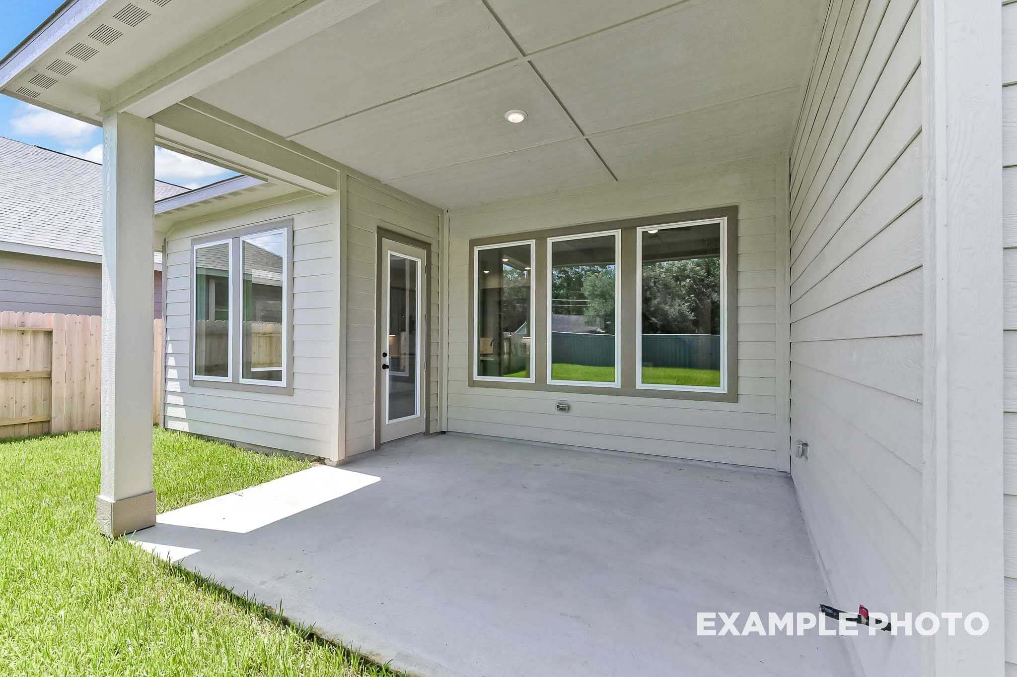 Spacious covered patio of The Sequoia home design featuring large windows, glass door, and lush green backyard in Crosby Texas