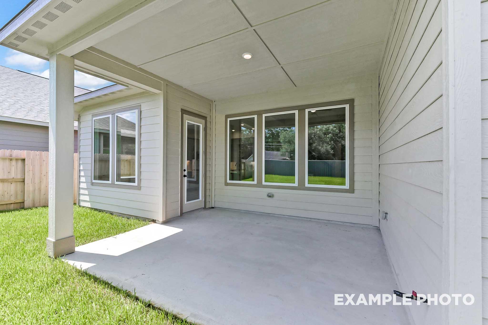 Spacious covered patio of The Sequoia home design featuring large windows, glass door, and lush green backyard in Crosby Texas