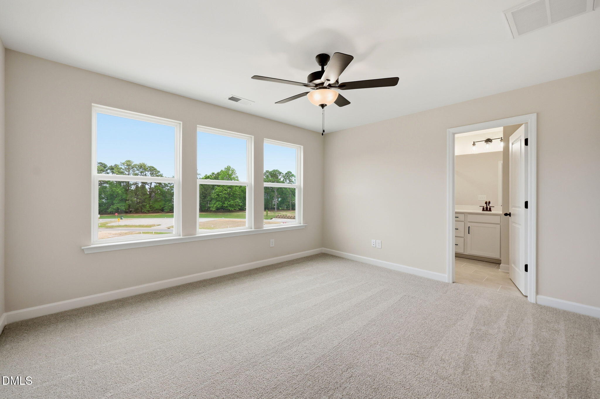 Bright bedroom with neutral carpet, ceiling fan, and en-suite bathroom in The Mitchell floor plan at Camden Park, NC.