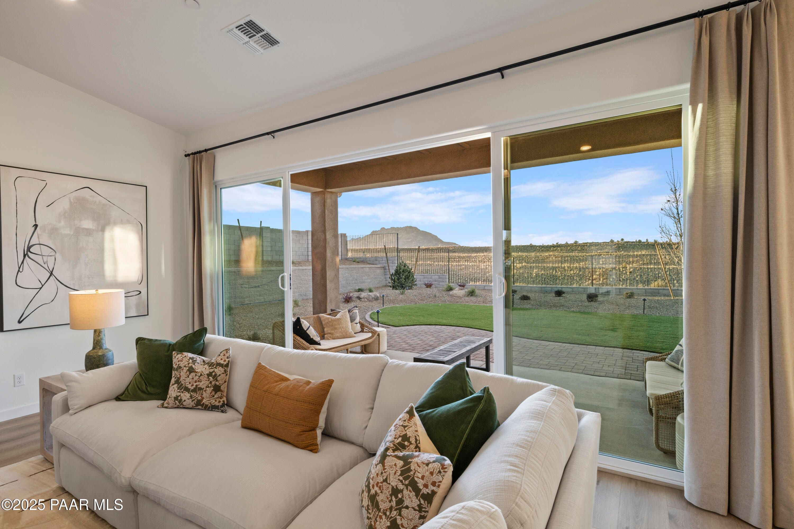 Cozy living room with beige sofa, sliding glass doors to covered patio, lush backyard and desert mountain view in Davidson Homes The Blaze D, Prescott Arizona