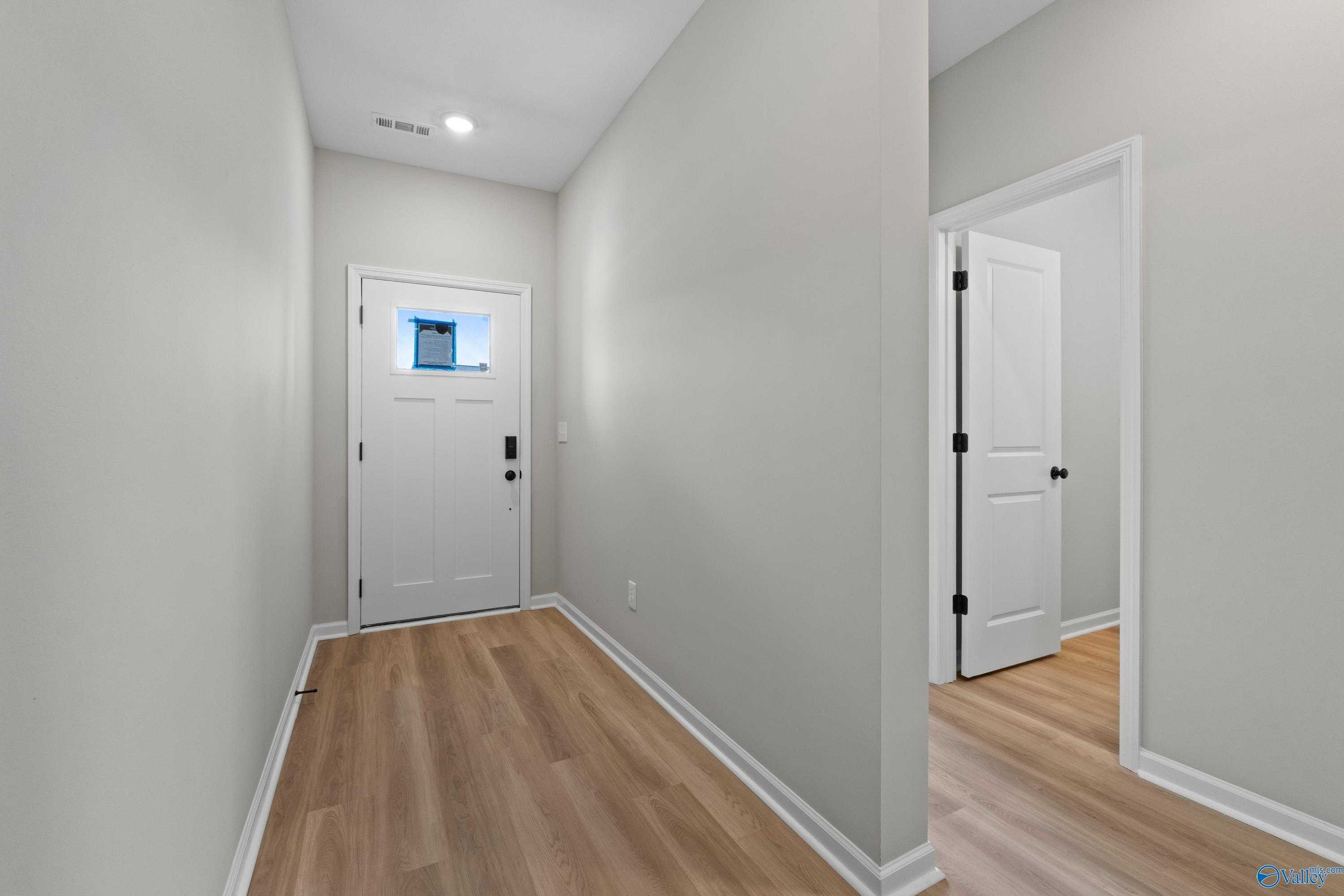 Bright entry hallway with white doors, light gray walls, and wood floors in The Phoenix 3-bedroom home, Hazel Green, Alabama