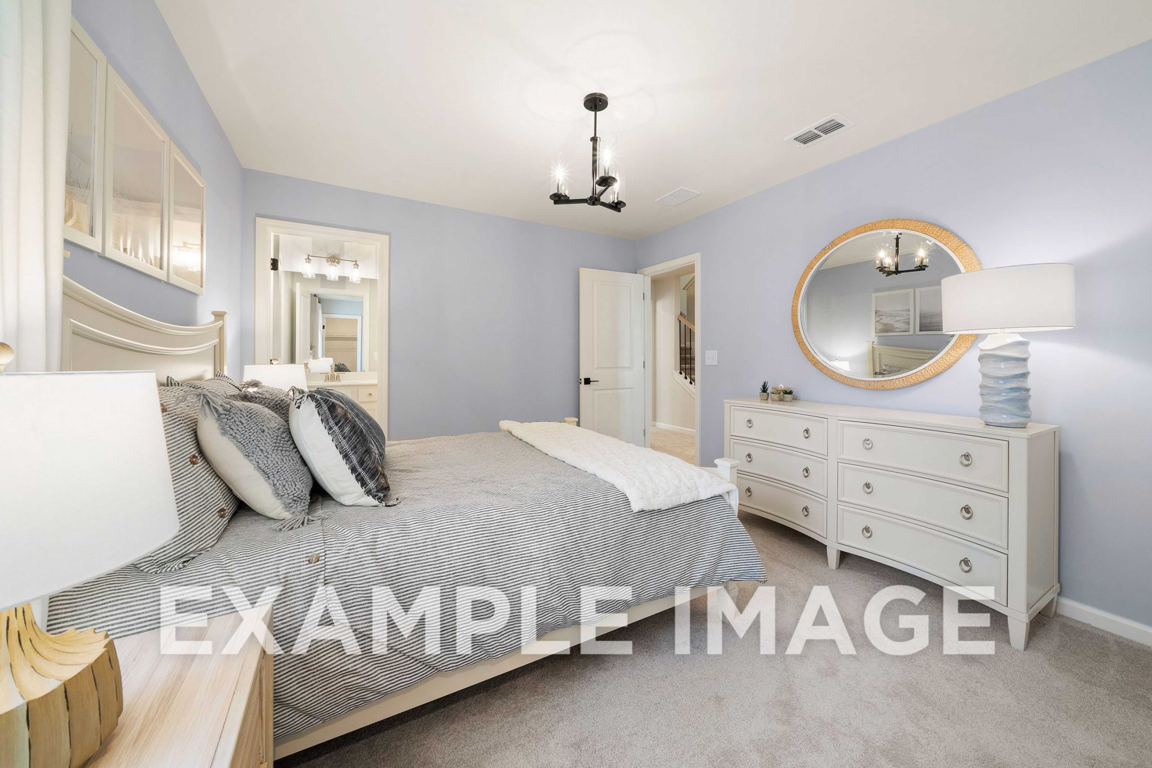 Spacious master bedroom in The Hickory A with light blue walls, king bed, white dresser, round mirror, and chandelier