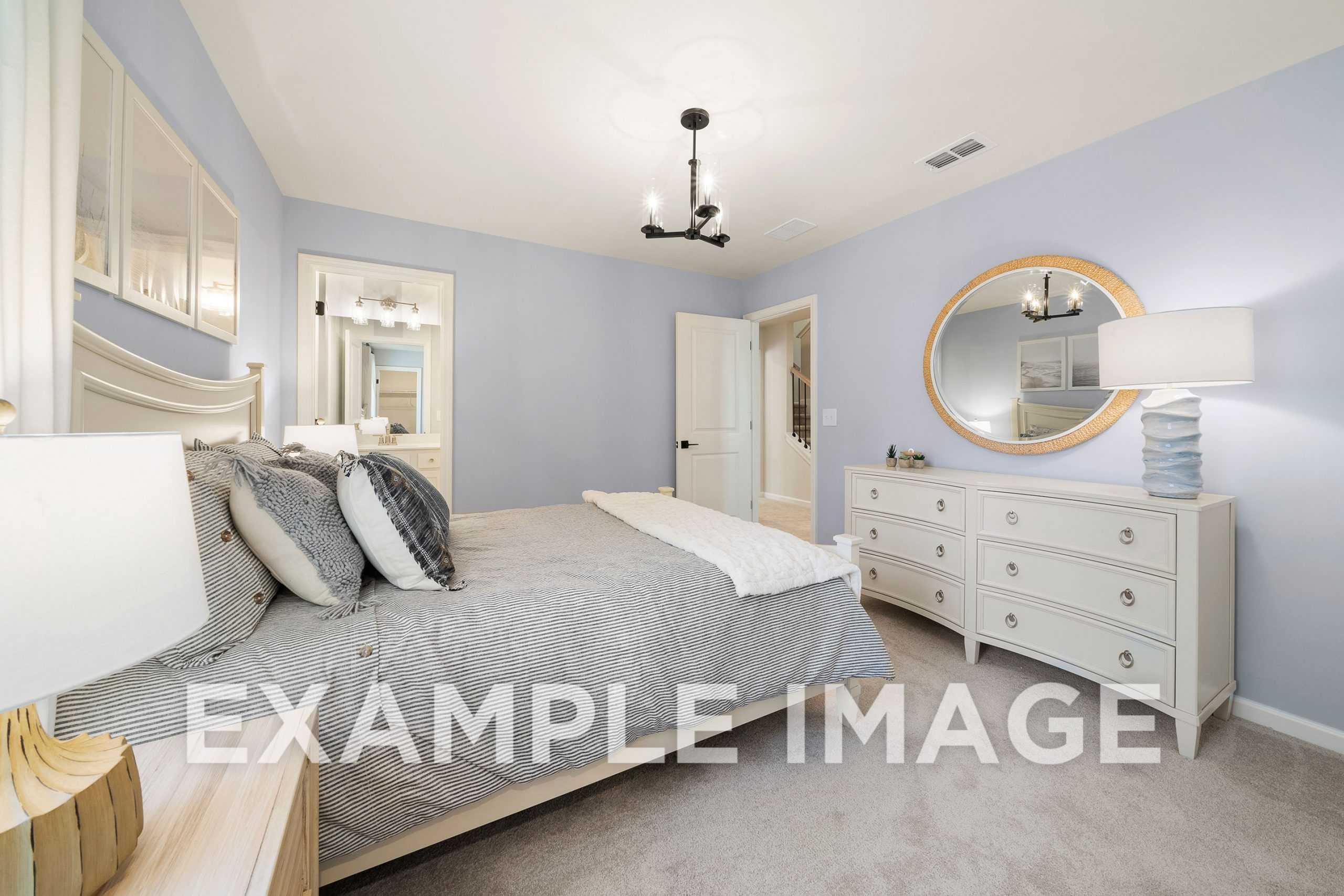 Spacious master bedroom in The Hickory A with light blue walls, king bed, white dresser, round mirror, and chandelier