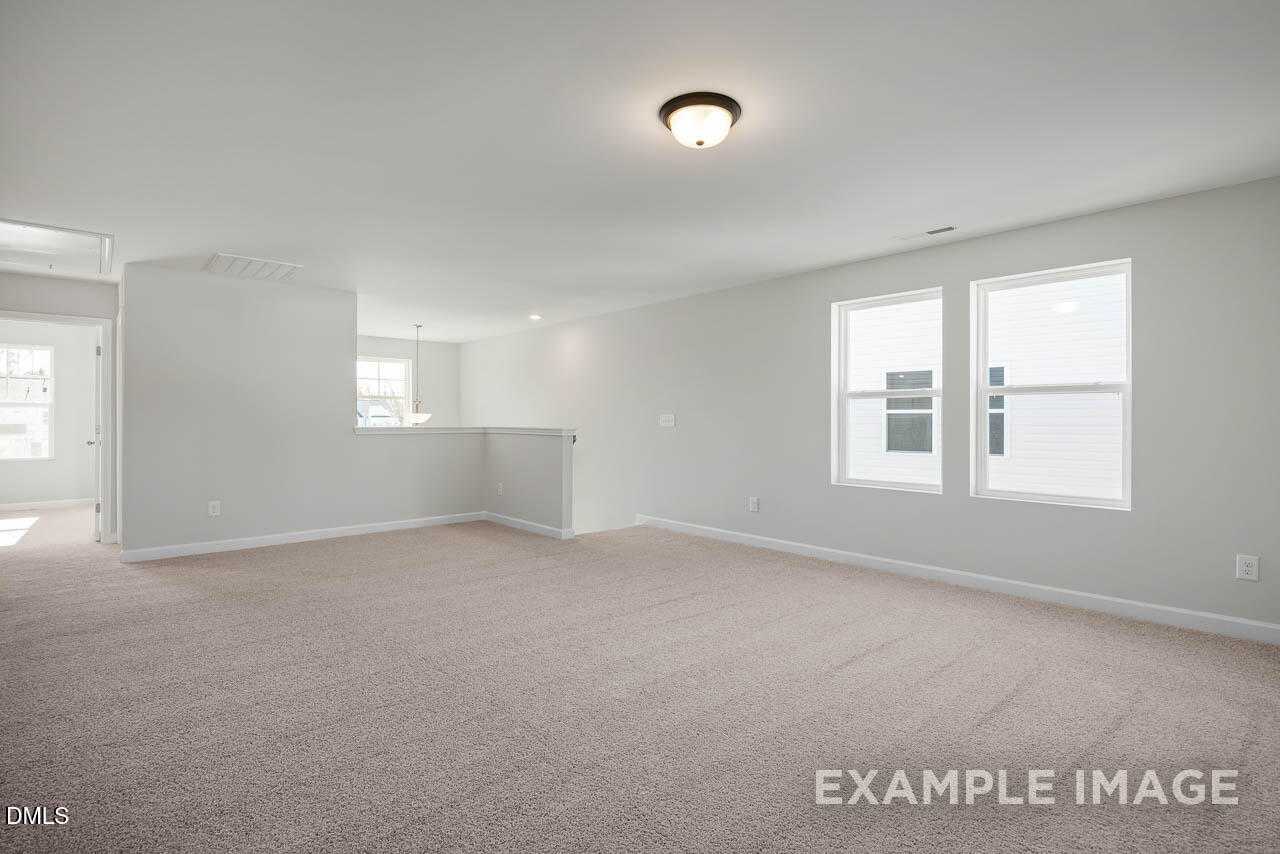 Spacious empty living room with beige carpet, neutral walls, large windows, and open layout in Davidson Homes The Adalynn A, Lillington, NC