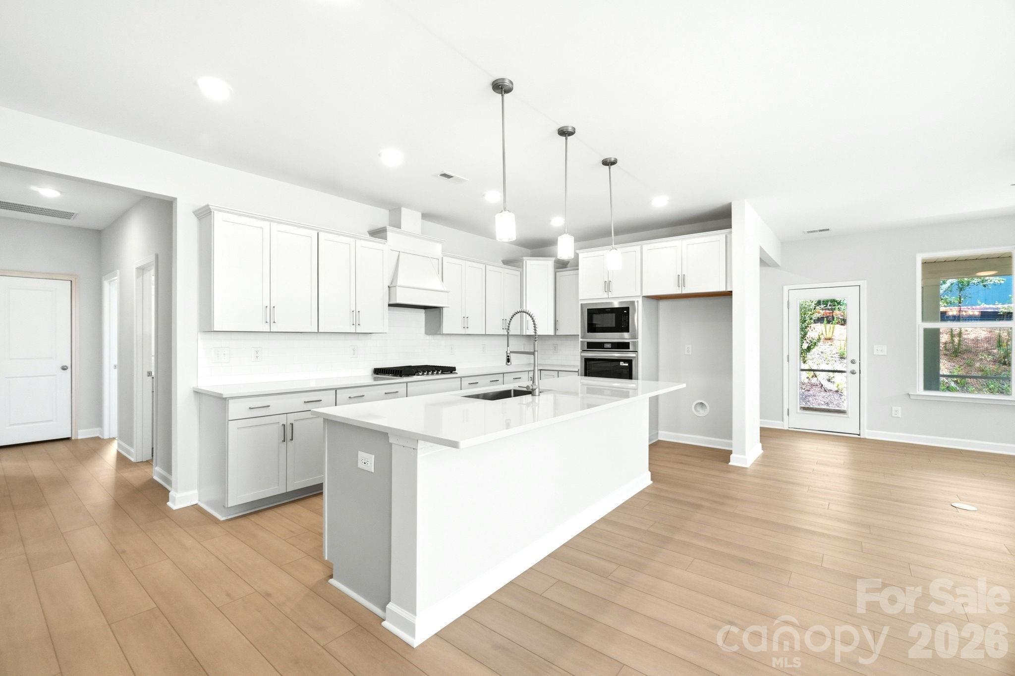 Modern white kitchen with quartz island, pendant lighting, and stainless appliances in The Magnolia B at Windgate, NC.