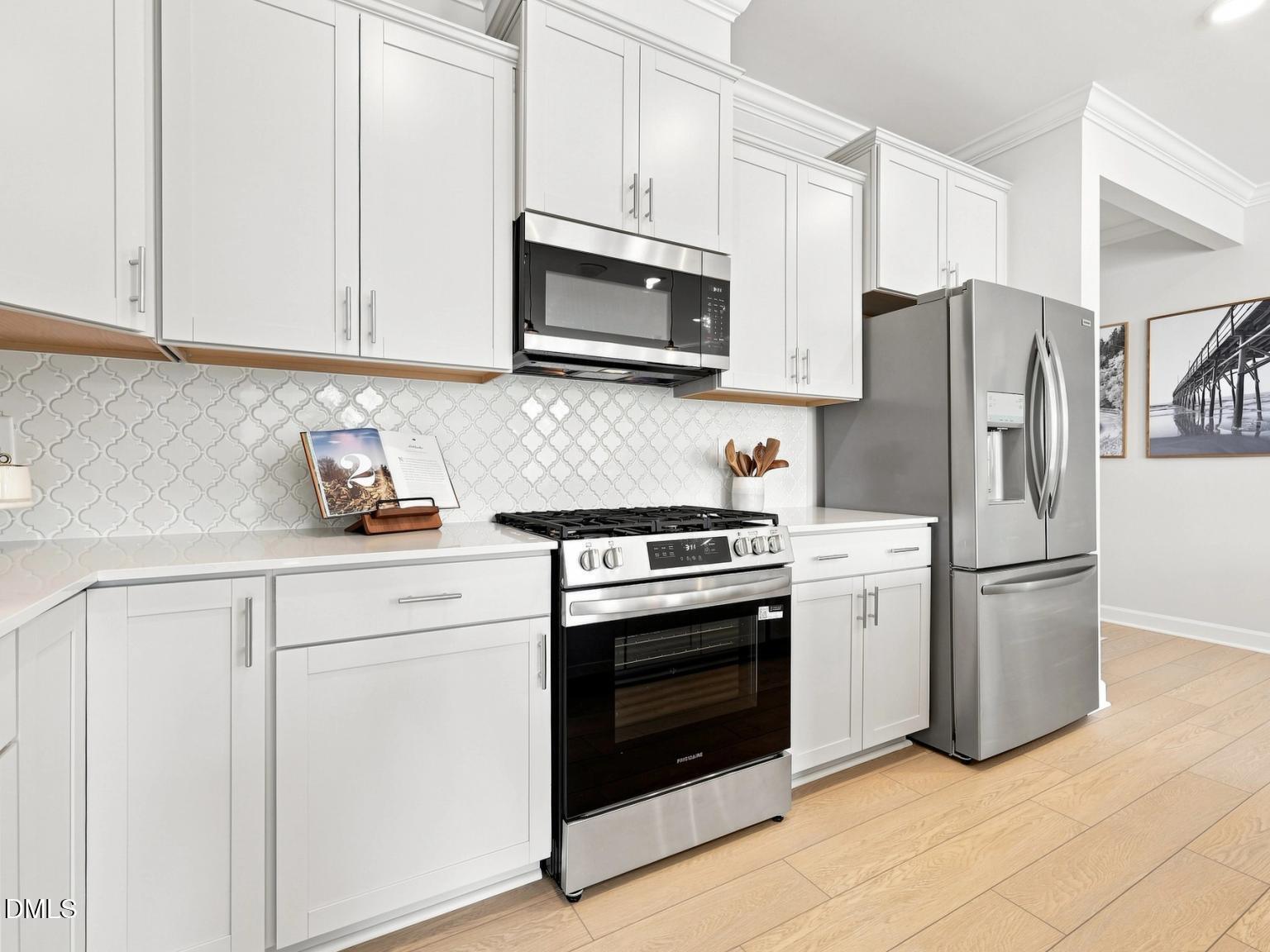 Modern kitchen with white cabinets, stainless steel appliances, and tile backsplash in The Daphne C, Woodland Crossing.