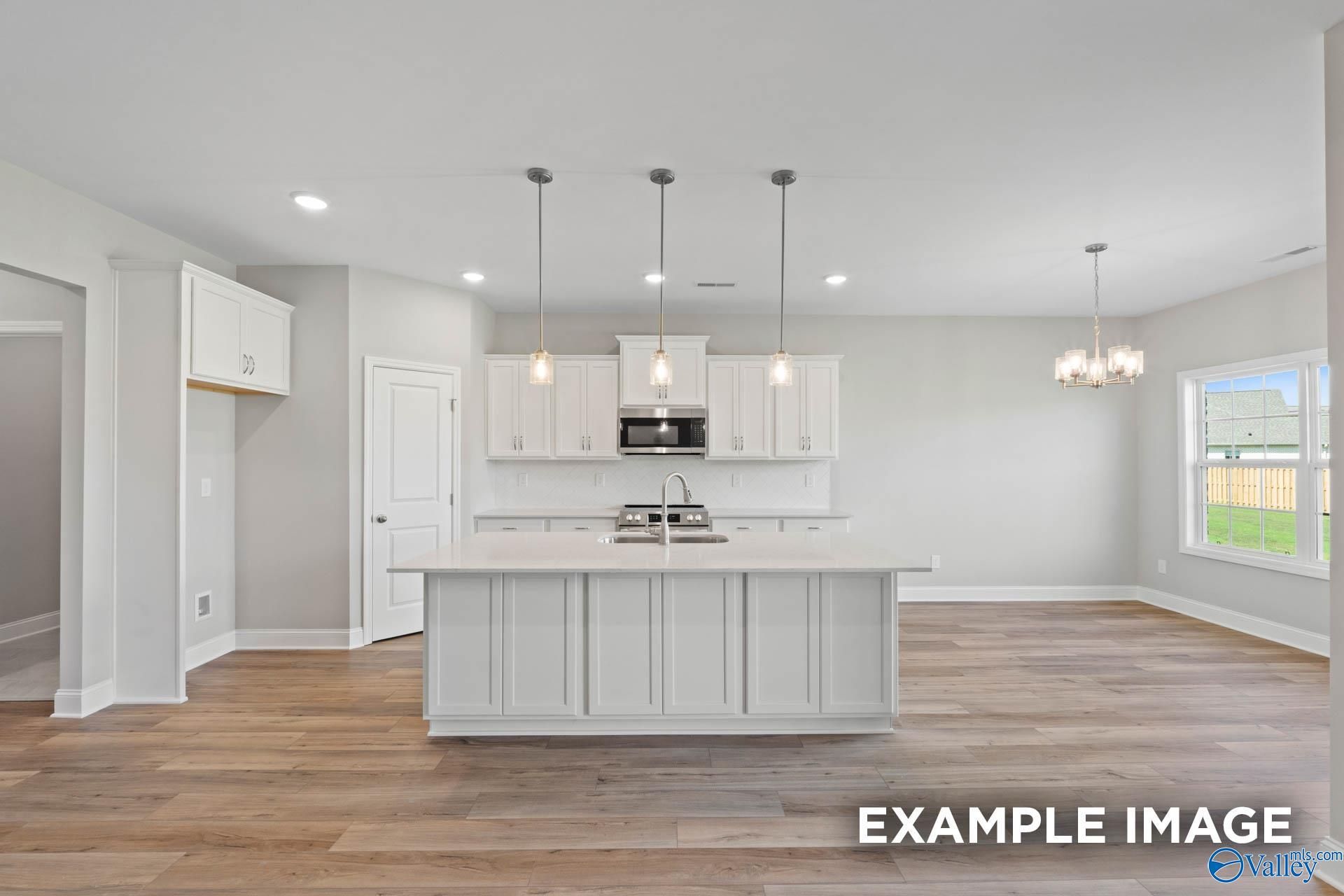 Modern white kitchen island with stainless appliances, pendant lights, and hardwood floors in Davidson Homes The Montgomery B, Hartselle, AL
