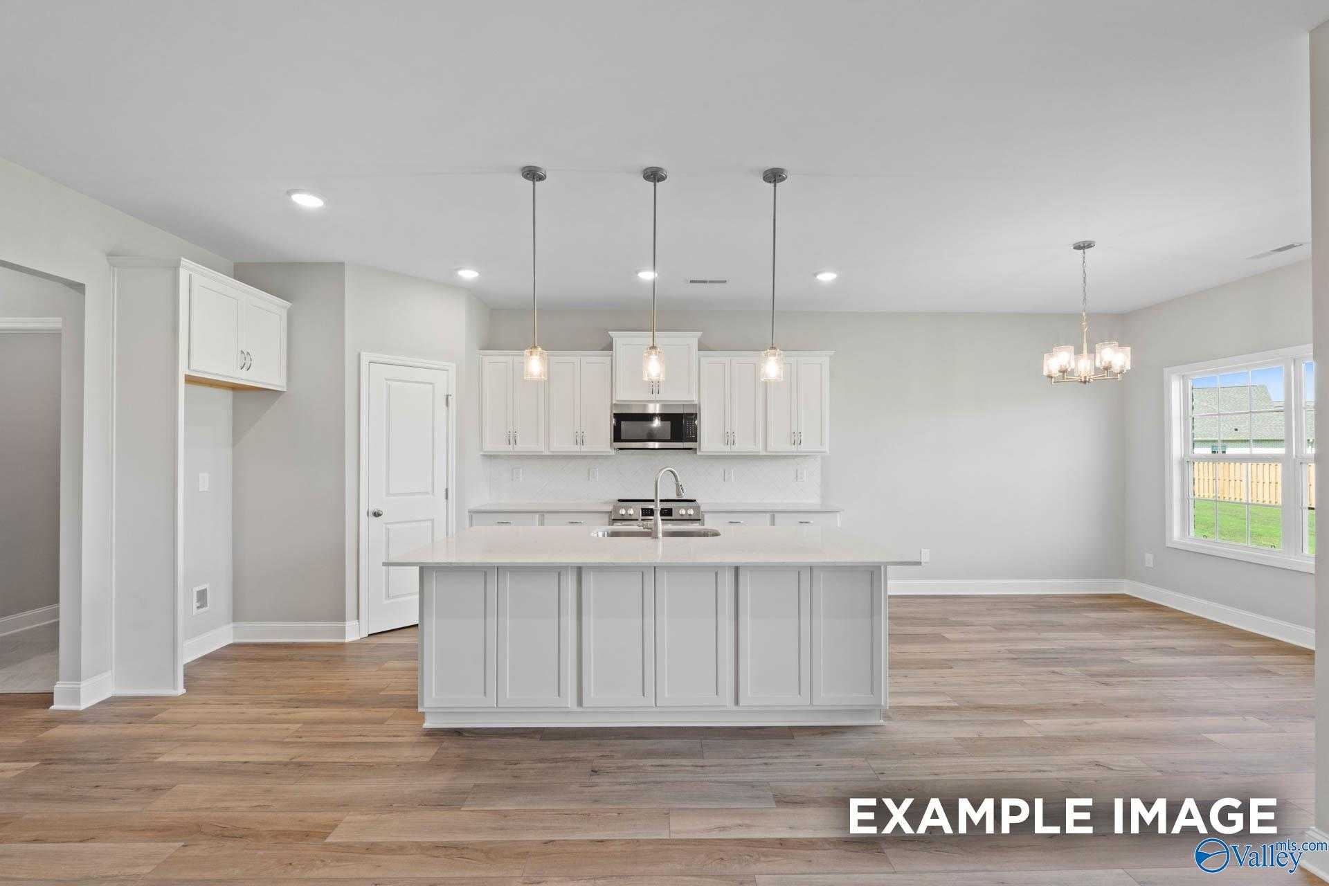 Modern white kitchen island with stainless appliances, pendant lights, and hardwood floors in Davidson Homes The Montgomery B, Hartselle, AL