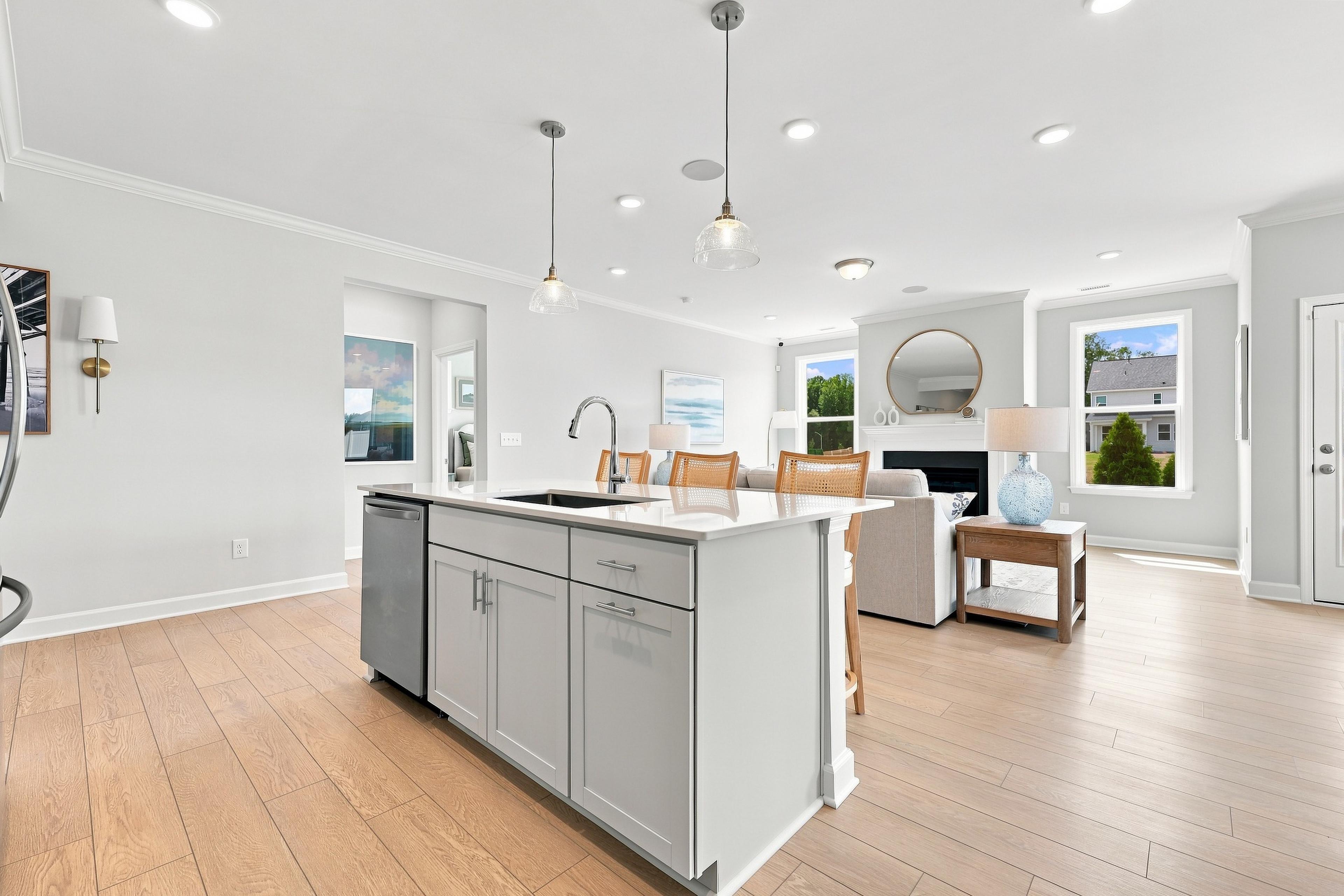 Open-concept kitchen and living area in The Daphne D featuring a large island, modern lighting, and hardwood flooring.