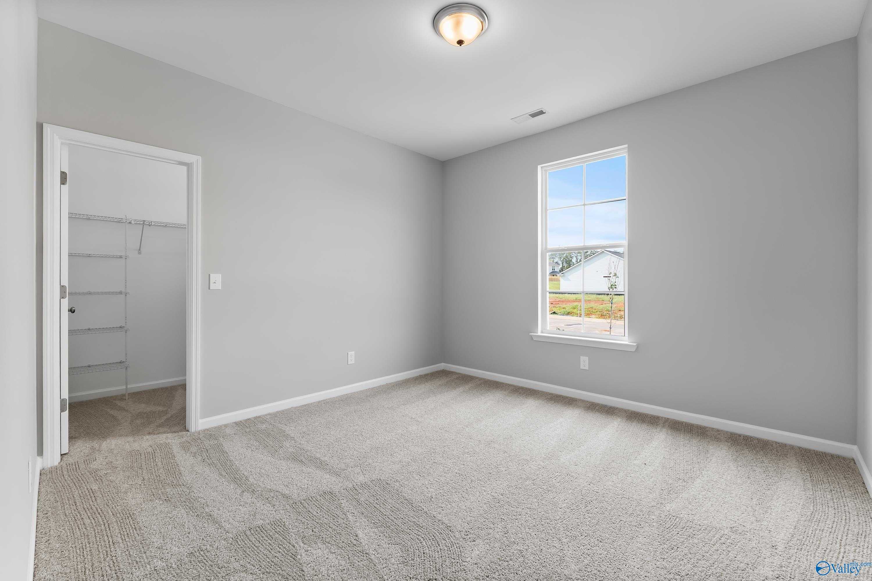 Spacious secondary bedroom with gray walls, carpet floor, walk-in closet, and large window in Evermore Homes The Grace, Madison, Alabama
