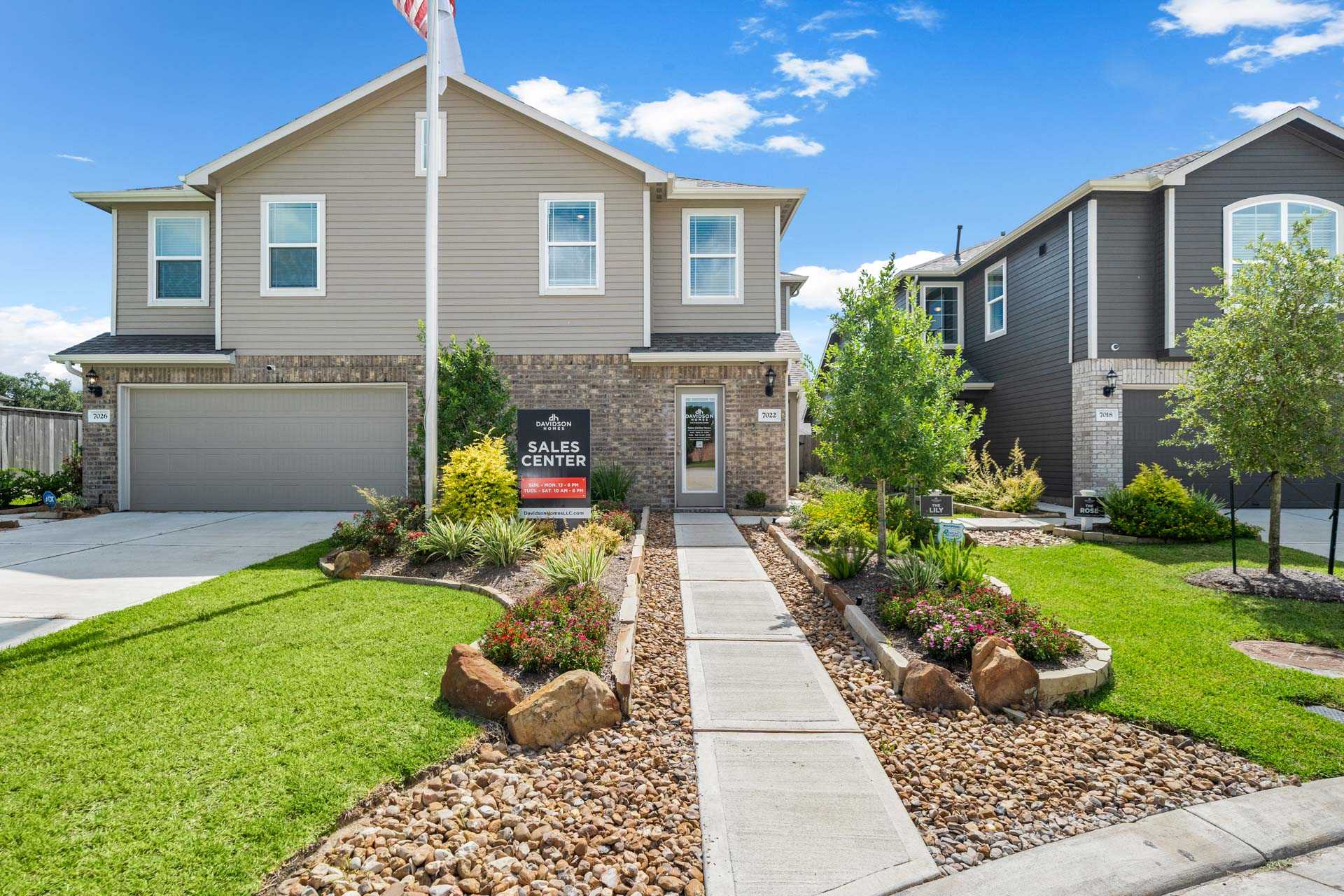 Model homes at Haven at Kieth Harrow in Cypress Texas with sales center sign, flagpole, stone pathway, and landscaped yards