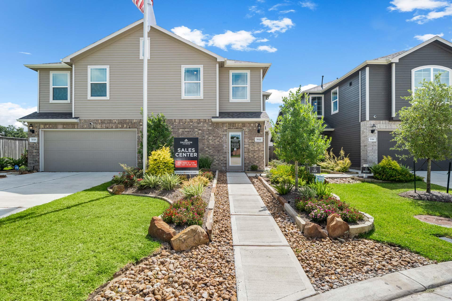 Model homes at Haven at Kieth Harrow in Cypress Texas with sales center sign, flagpole, stone pathway, and landscaped yards