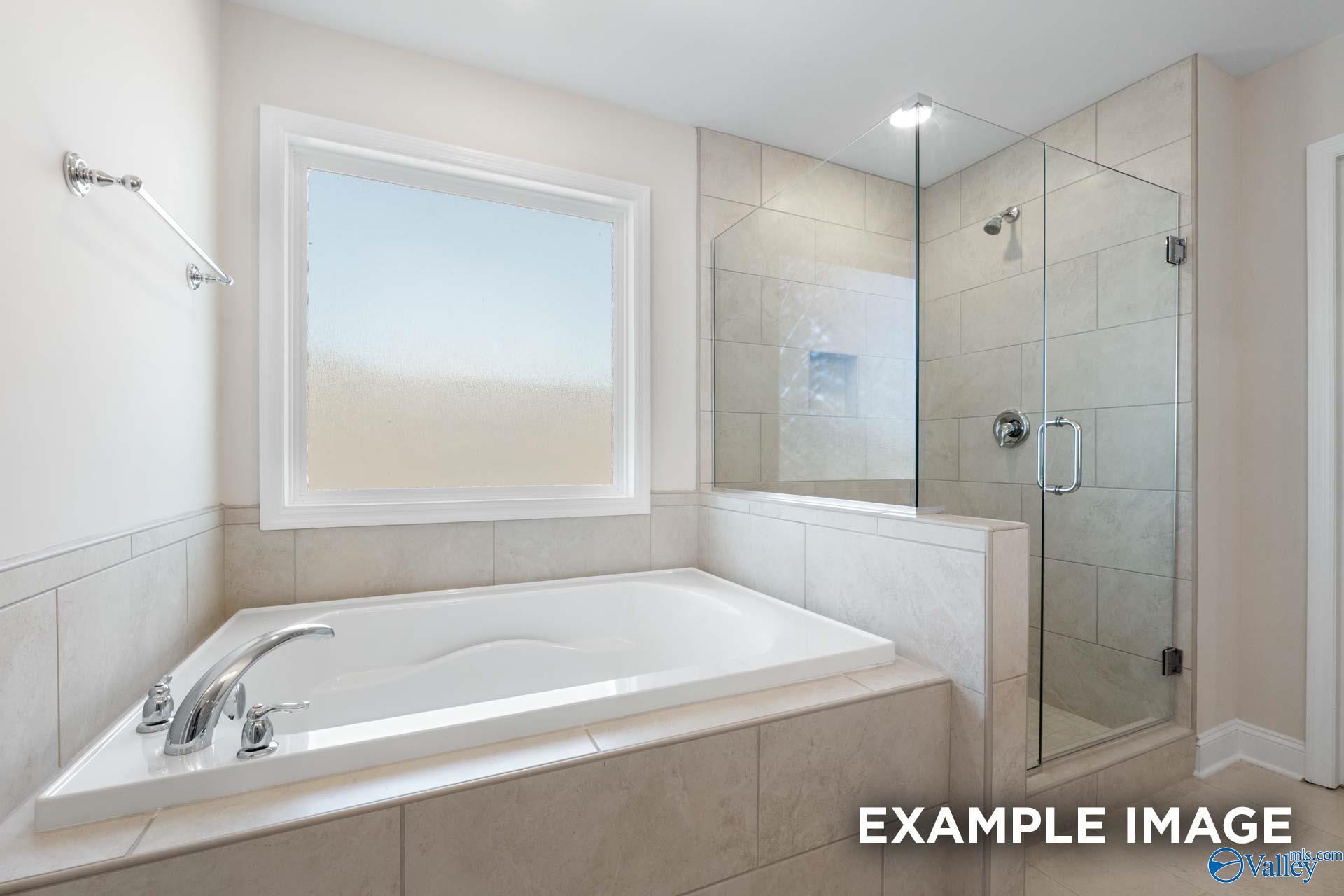 Elegant master bathroom with corner soaking tub, frameless glass shower, and frosted window in Davidson Homes Madison A, Toney Alabama