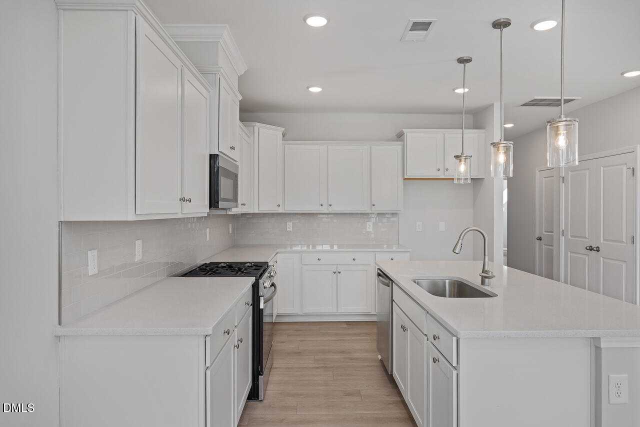Modern white kitchen with quartz island, stainless steel appliances, and pendant lights in Davidson Homes The Graham, Fuquay-Varina, NC