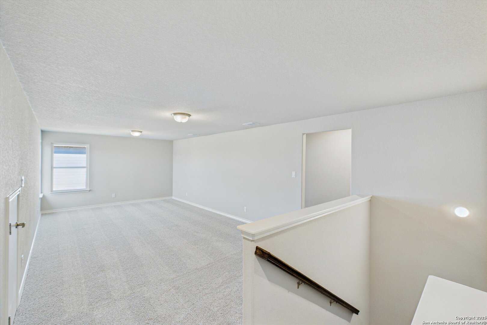 Spacious carpeted upstairs loft with window, open doorway, and staircase in 5-bedroom Davidson Homes Jennings H, Ladera, San Antonio