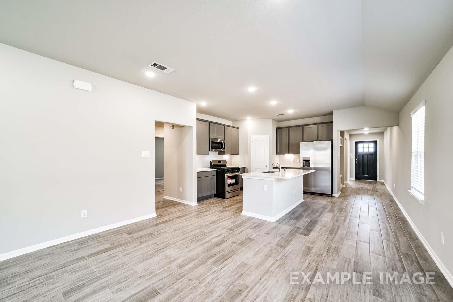 Open-concept kitchen with grey cabinets and island in The Riviera A floor plan at Emberly in Beasley, Texas.