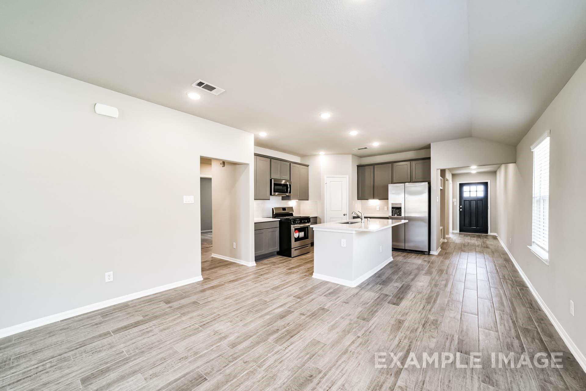 Open-concept kitchen with grey cabinets and island in The Riviera A floor plan at Emberly in Beasley, Texas.