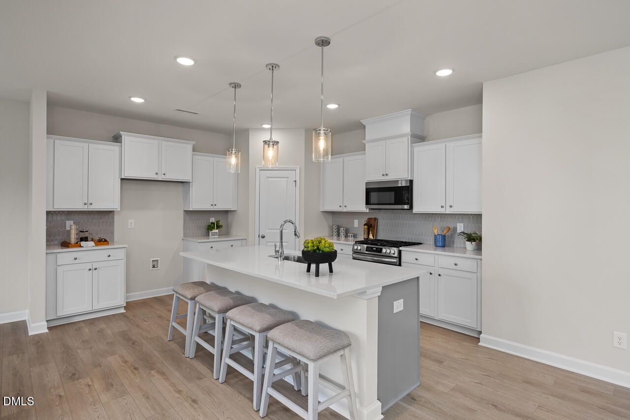 Modern white kitchen with granite island, stainless appliances, pendant lights in The Preston A by Davidson Homes, Lillington, NC
