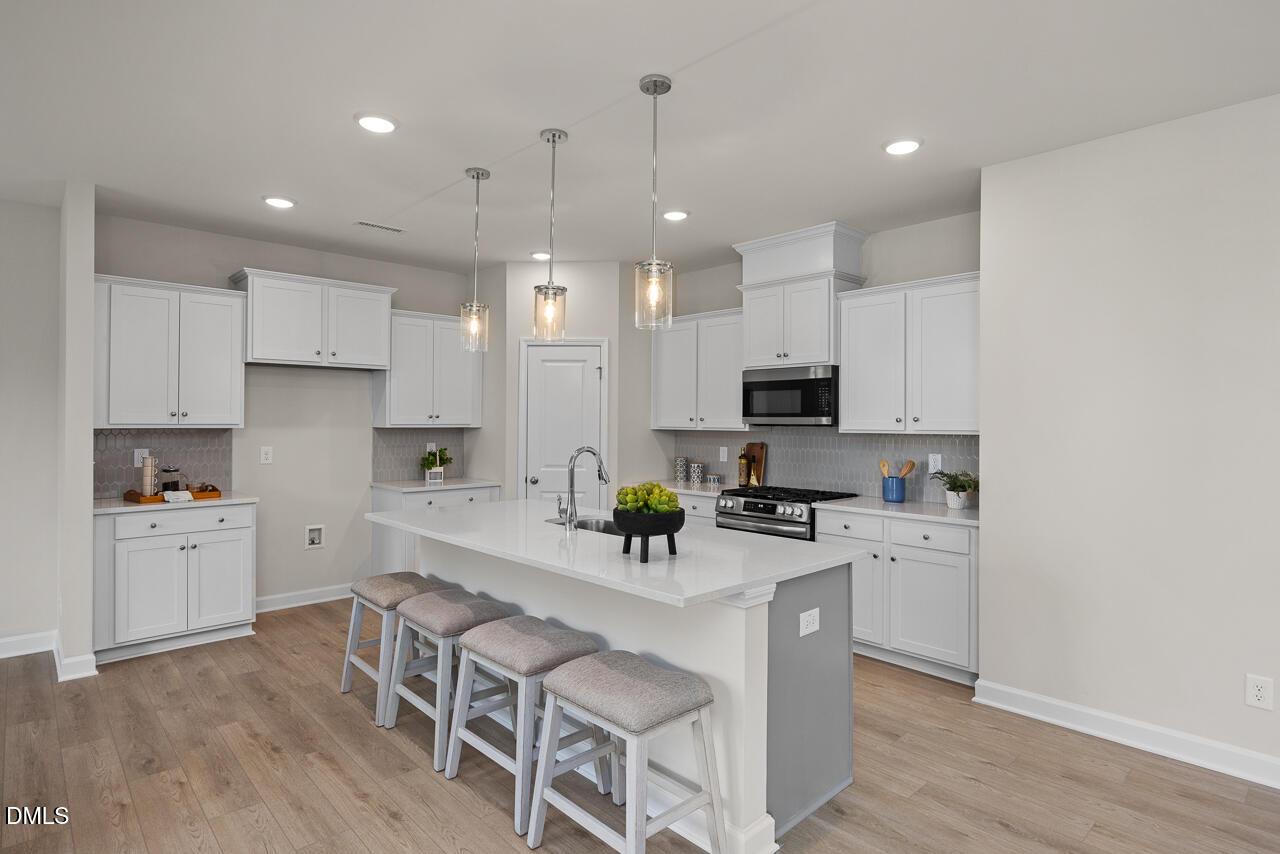 Modern white kitchen with granite island, stainless appliances, pendant lights in The Preston A by Davidson Homes, Lillington, NC