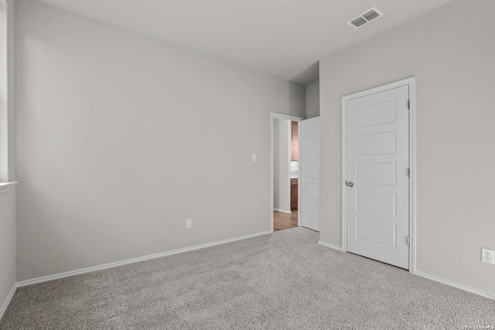 Spacious secondary bedroom with light gray walls, beige carpet, and adjacent bath in Davidson Homes The Frio B, San Antonio