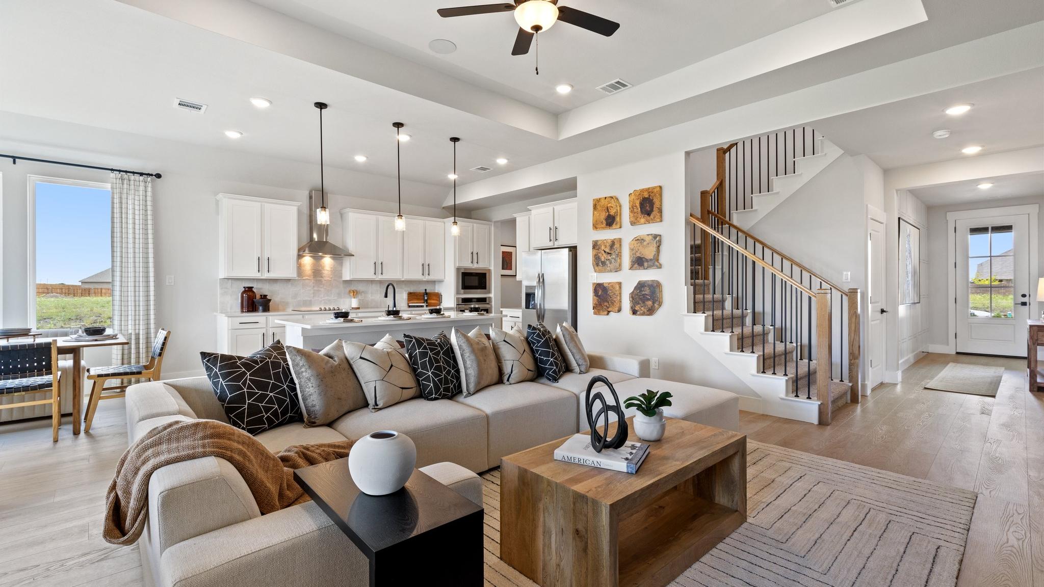 Open-concept living room and kitchen in Mercer Meadows Royse City TX home with hardwood floors, white cabinetry, ceiling fan, and staircase