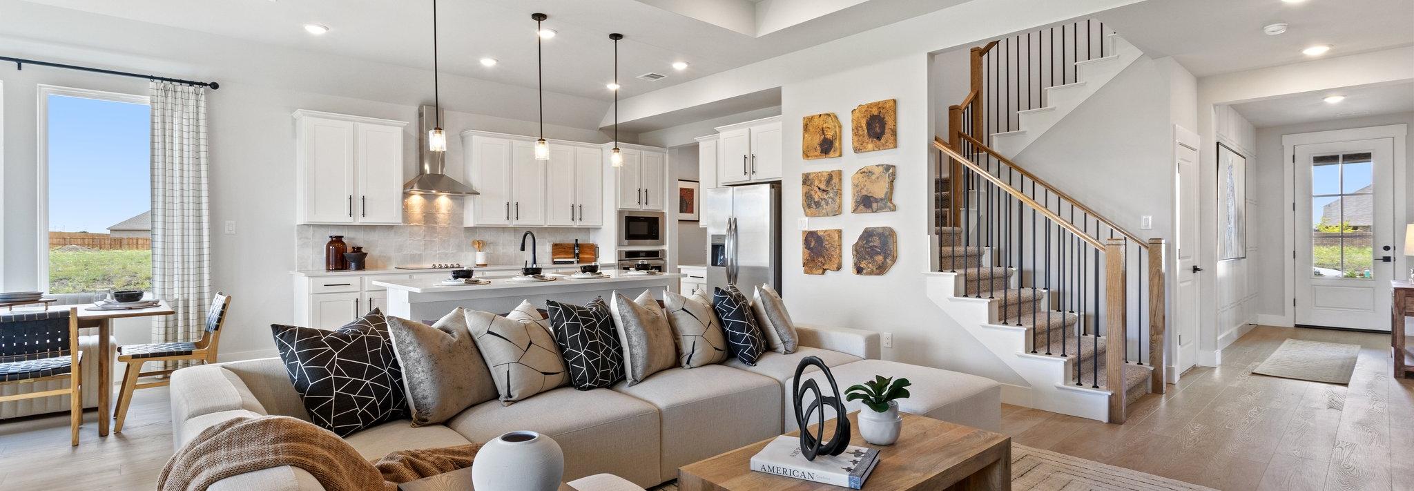 Open-concept living room and kitchen in Mercer Meadows Royse City TX home with hardwood floors, white cabinetry, ceiling fan, and staircase