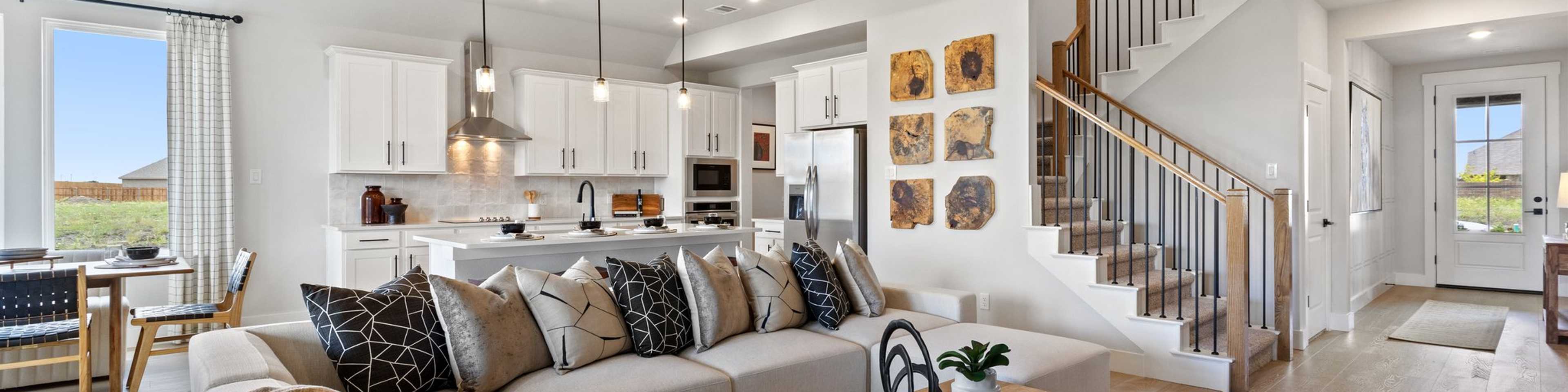 Open-concept living room and kitchen in Mercer Meadows Royse City TX home with hardwood floors, white cabinetry, ceiling fan, and staircase