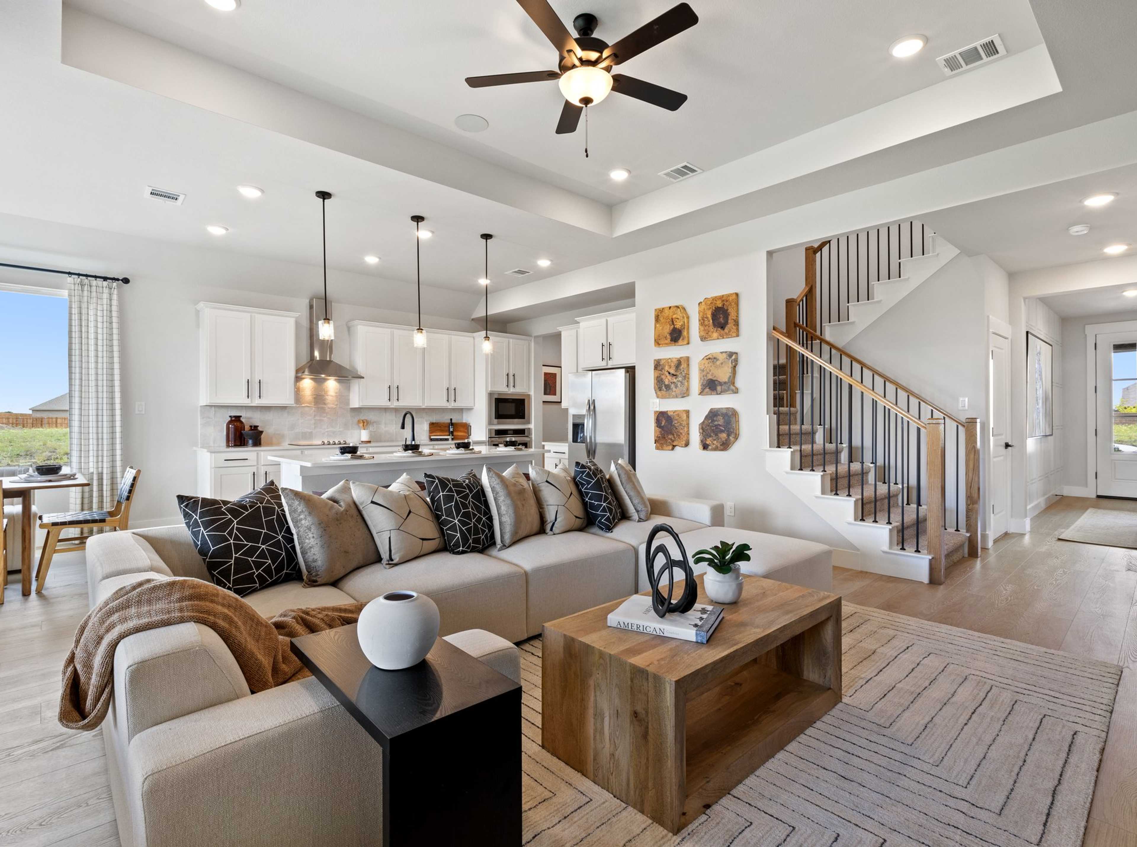 Open-concept living room and kitchen in Mercer Meadows Royse City TX home with hardwood floors, white cabinetry, ceiling fan, and staircase