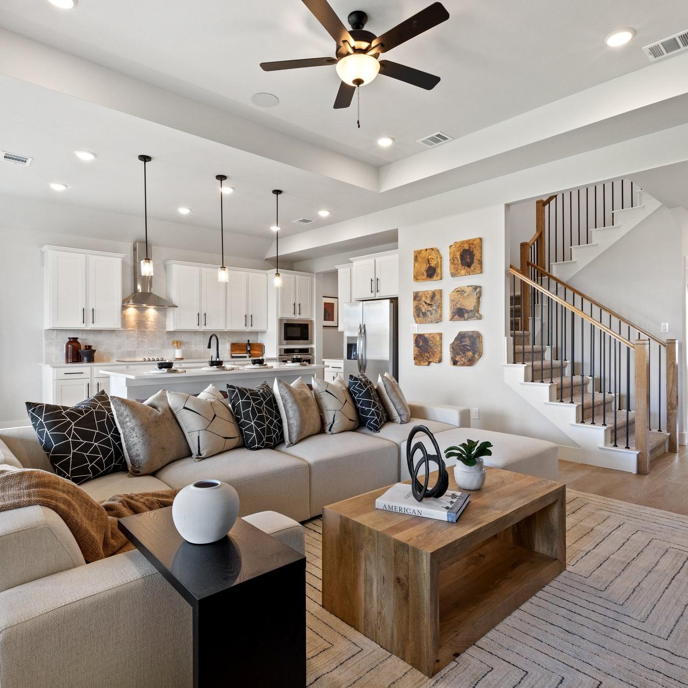 Open-concept living room and kitchen in Mercer Meadows Royse City TX home with hardwood floors, white cabinetry, ceiling fan, and staircase
