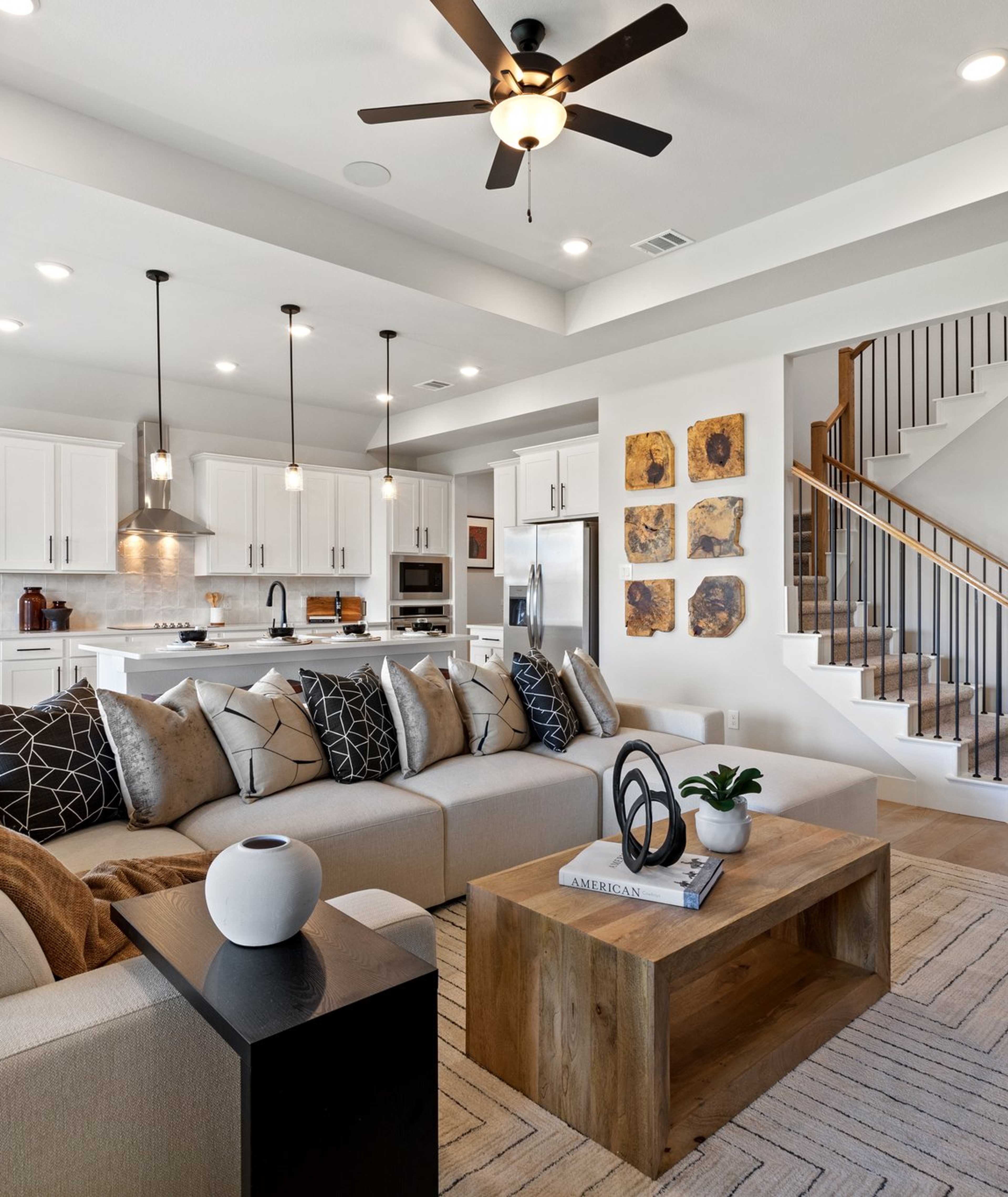 Open-concept living room and kitchen in Mercer Meadows Royse City TX home with hardwood floors, white cabinetry, ceiling fan, and staircase