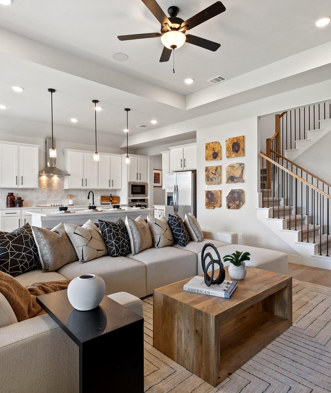 Open-concept living room and kitchen in Mercer Meadows Royse City TX home with hardwood floors, white cabinetry, ceiling fan, and staircase