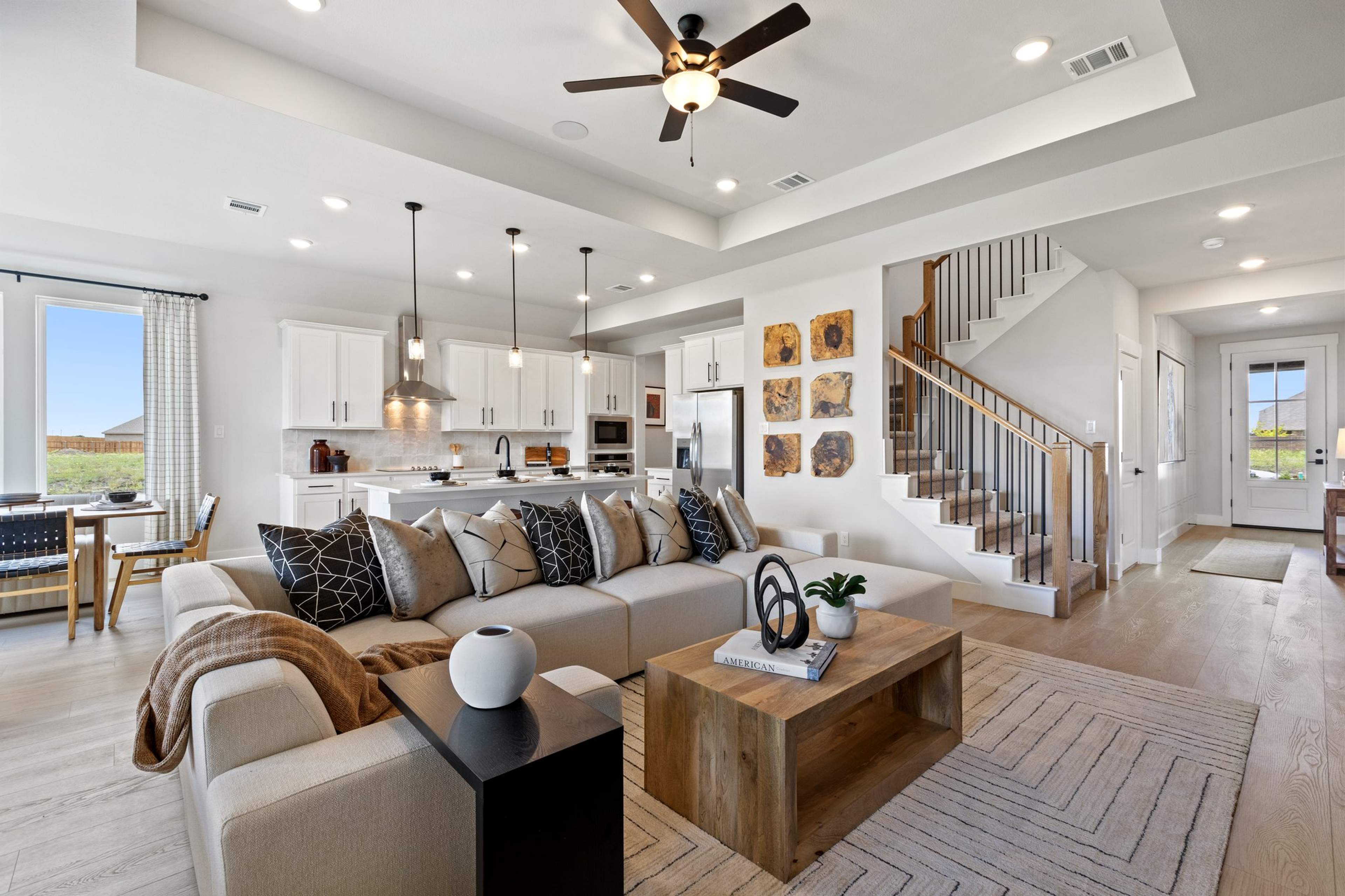 Open-concept living room and kitchen in Mercer Meadows Royse City TX home with hardwood floors, white cabinetry, ceiling fan, and staircase