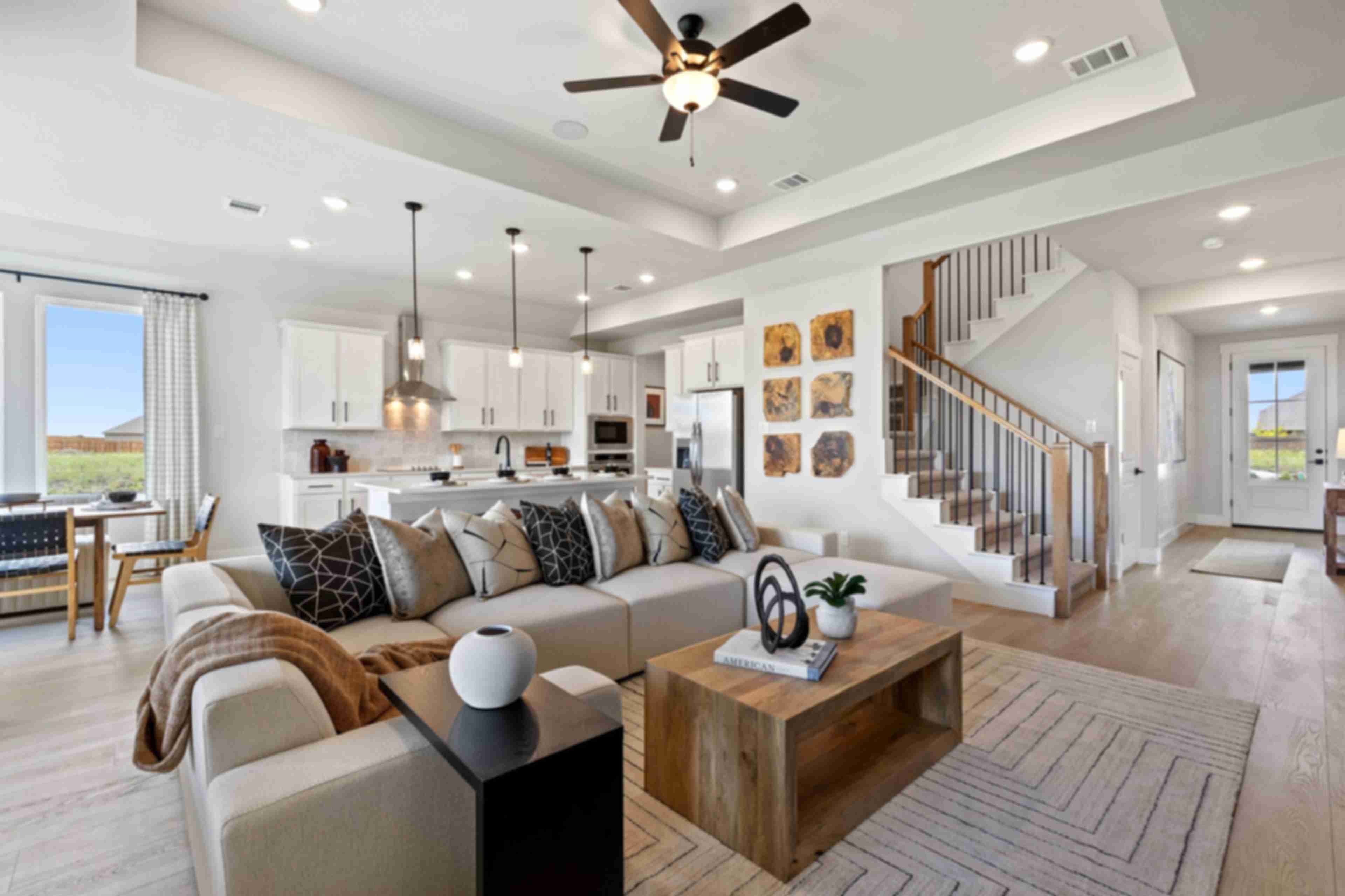 Open-concept living room and kitchen in Mercer Meadows Royse City TX home with hardwood floors, white cabinetry, ceiling fan, and staircase