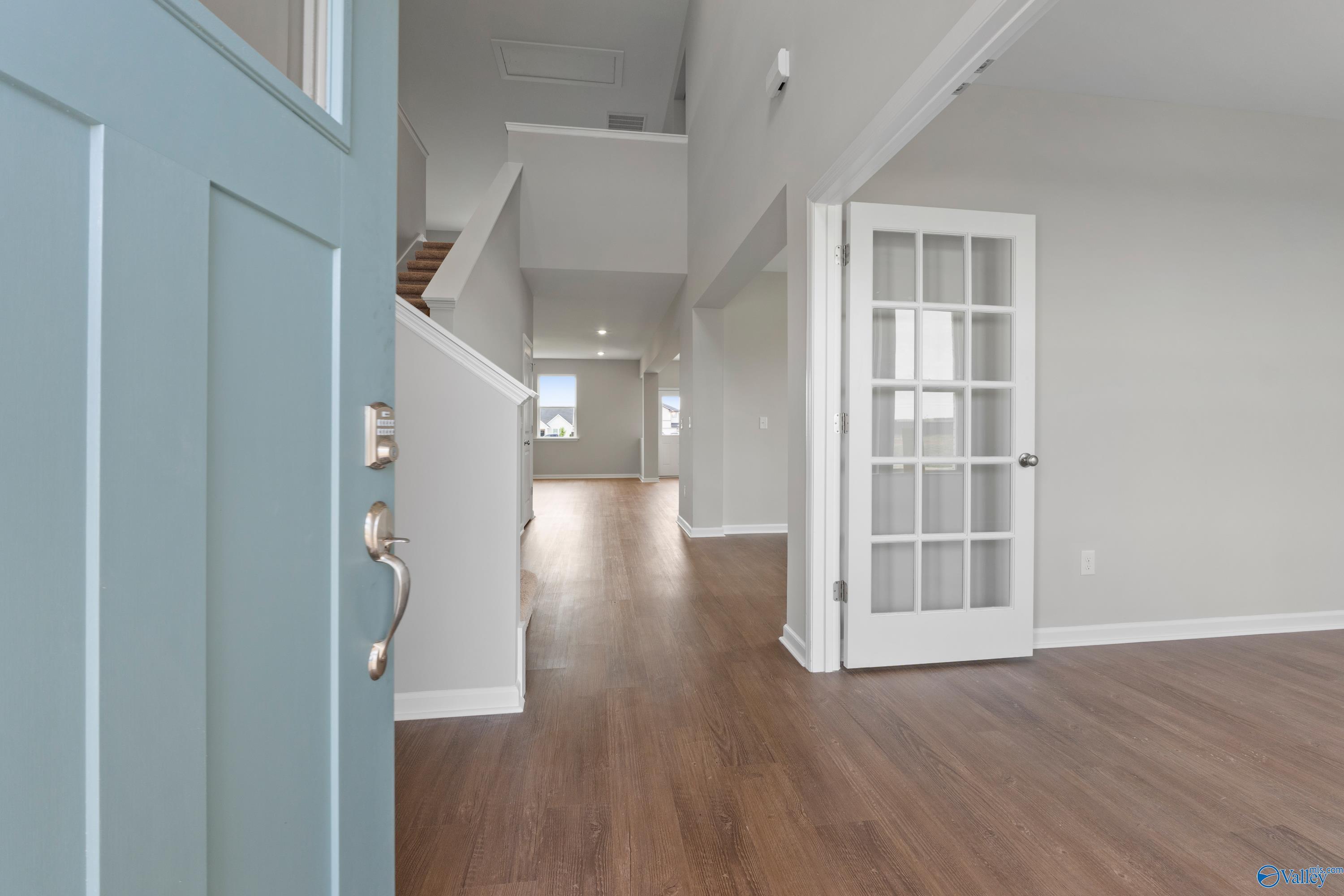 Inviting entryway with open blue door, hardwood floors, grand staircase, and glass-paneled door in Davidson Homes The Dorado, Athens AL