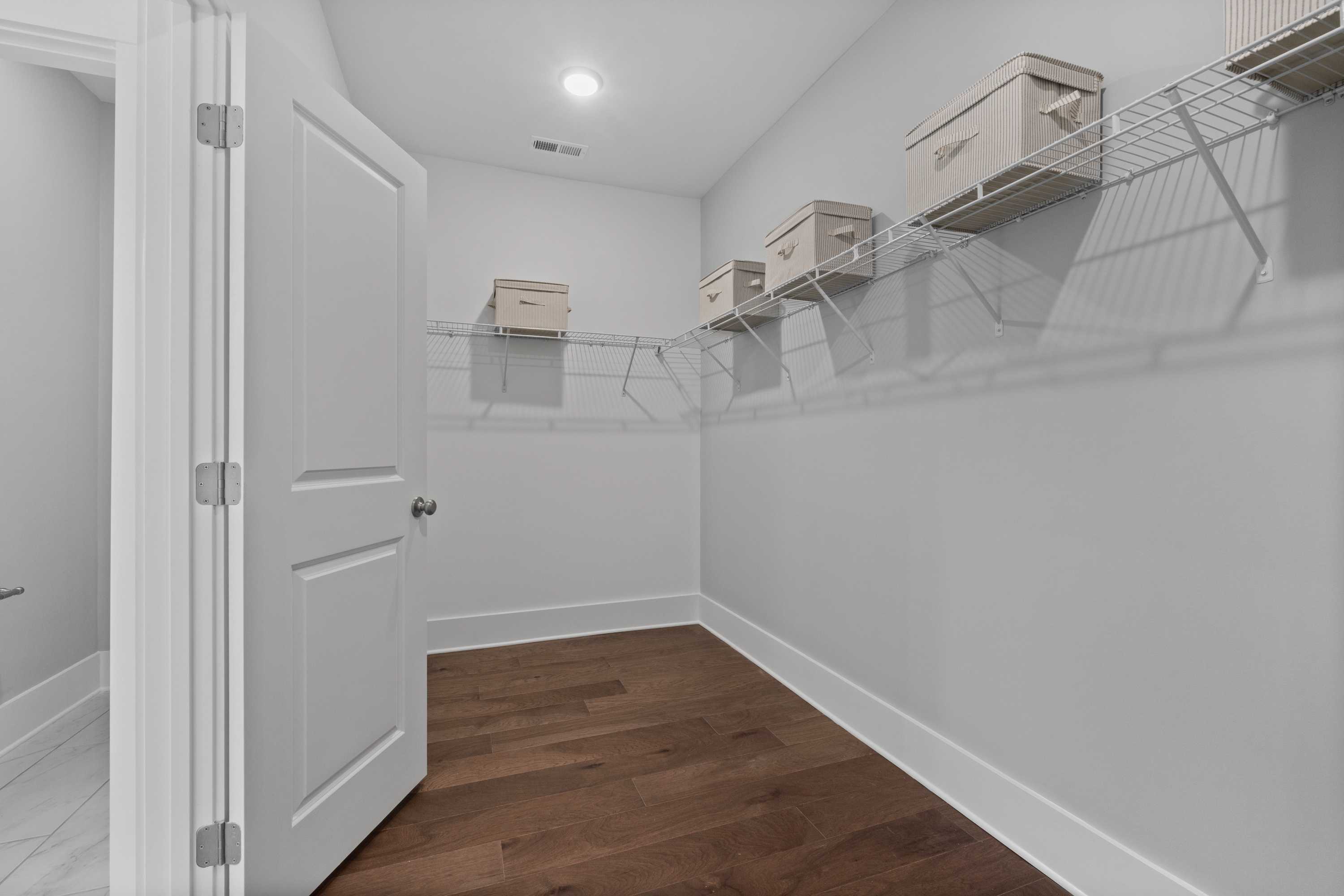 Spacious walk-in closet at Creekside in Harvest Alabama with wire shelving, beige storage bins, hardwood floors