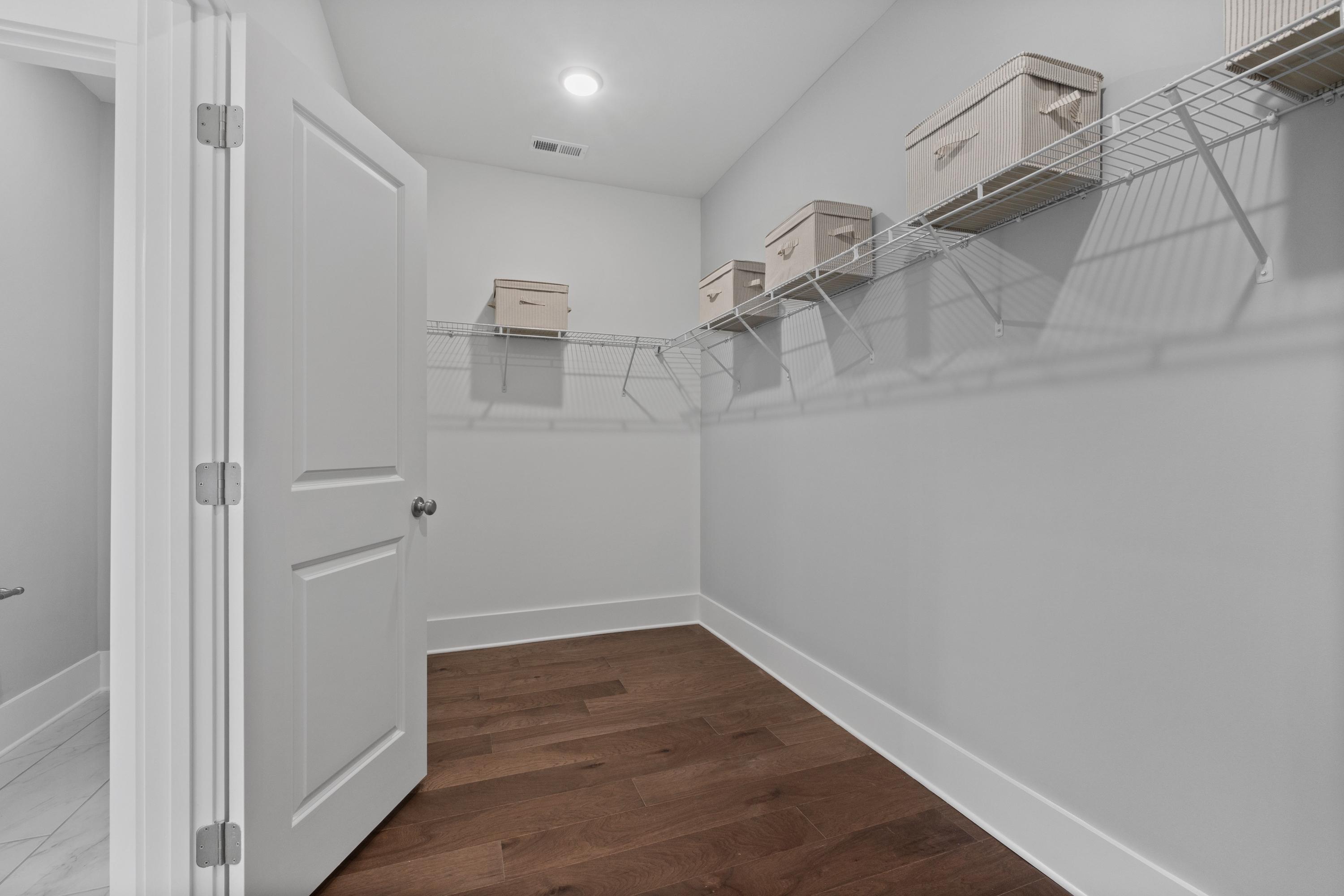 Spacious walk-in closet at Creekside in Harvest Alabama with wire shelving, beige storage bins, hardwood floors