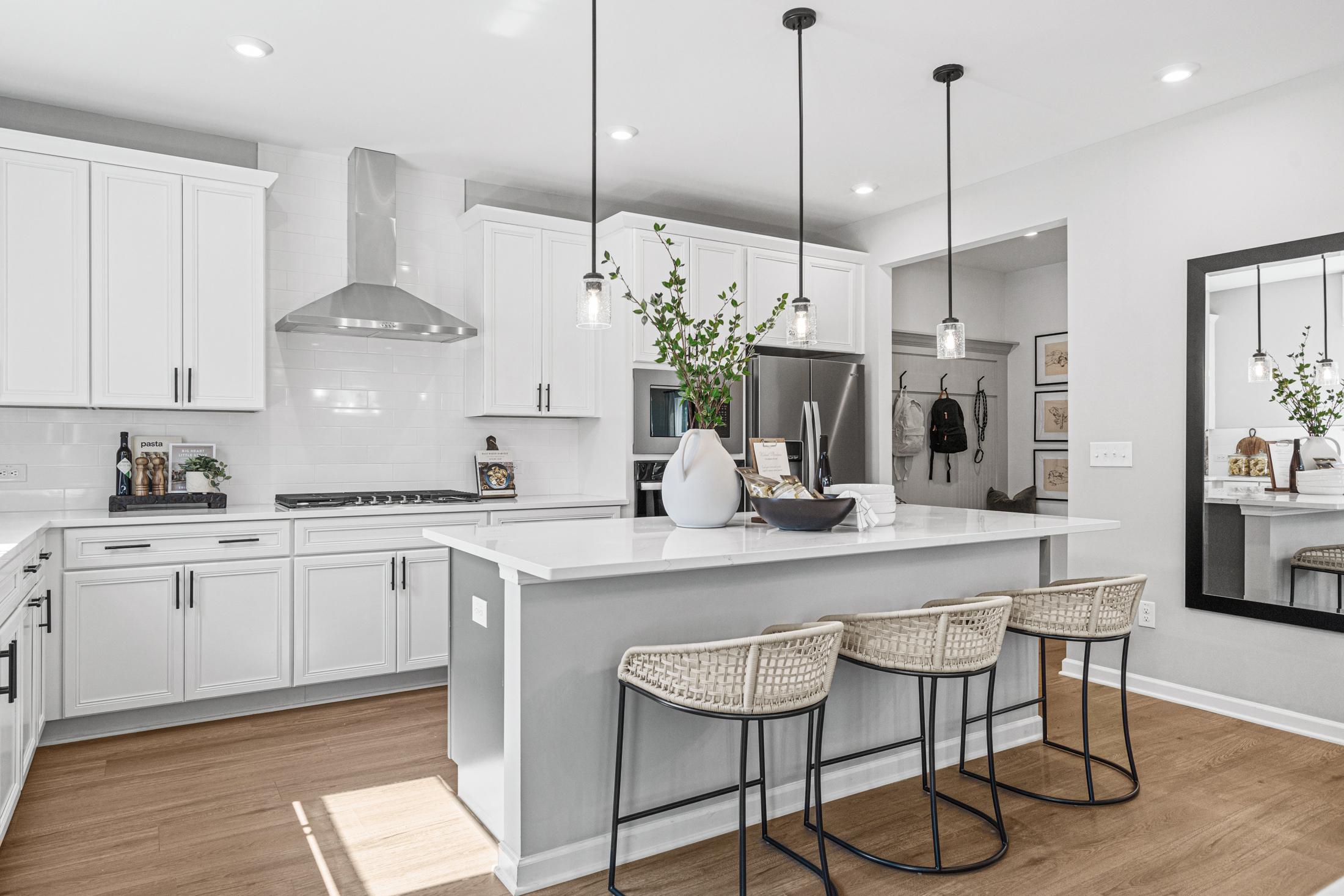 Modern kitchen in The Hickory B featuring white shaker cabinets, large quartz island with rattan bar stools, stainless steel appliances, pendant lights