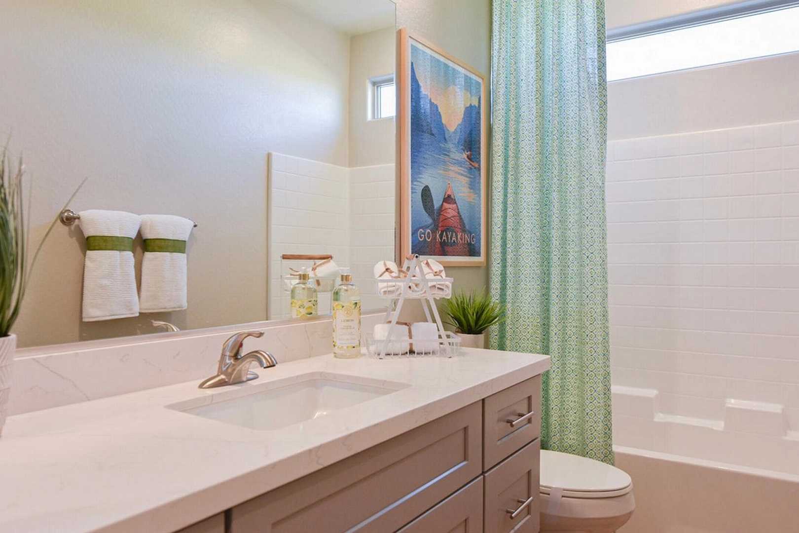 Spacious bathroom at North Ridge Pronghorn Ranch in Prescott Valley AZ with white quartz vanity, gray cabinets, green shower curtain, potted plants, and framed artwork
