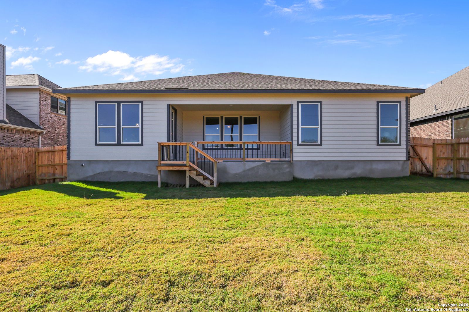 Back exterior of The Jennings G 2-story home with covered porch, large windows, wooden deck stairs, and fenced grassy yard in Castroville, Texas