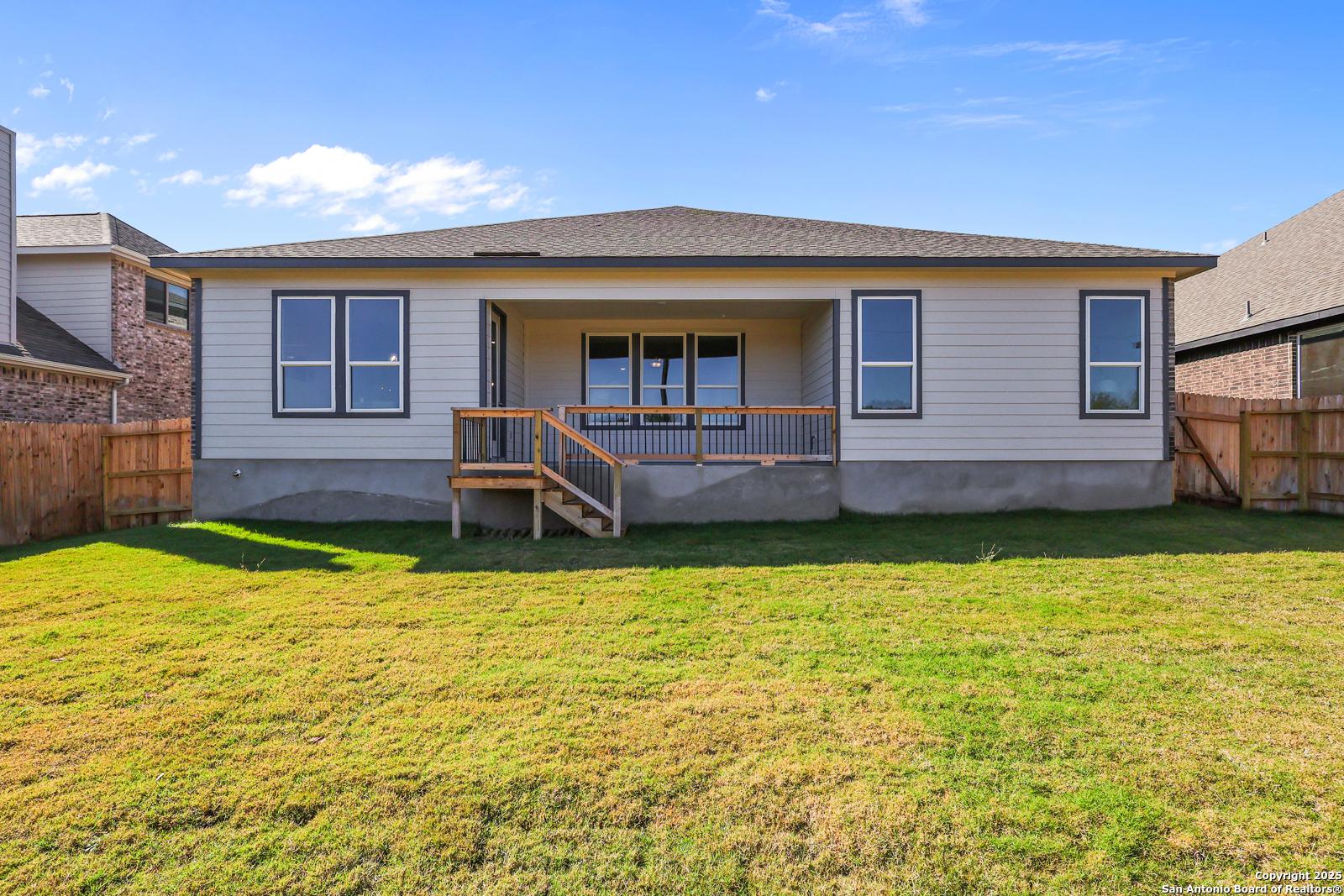 Back exterior of The Jennings G 2-story home with covered porch, large windows, wooden deck stairs, and fenced grassy yard in Castroville, Texas