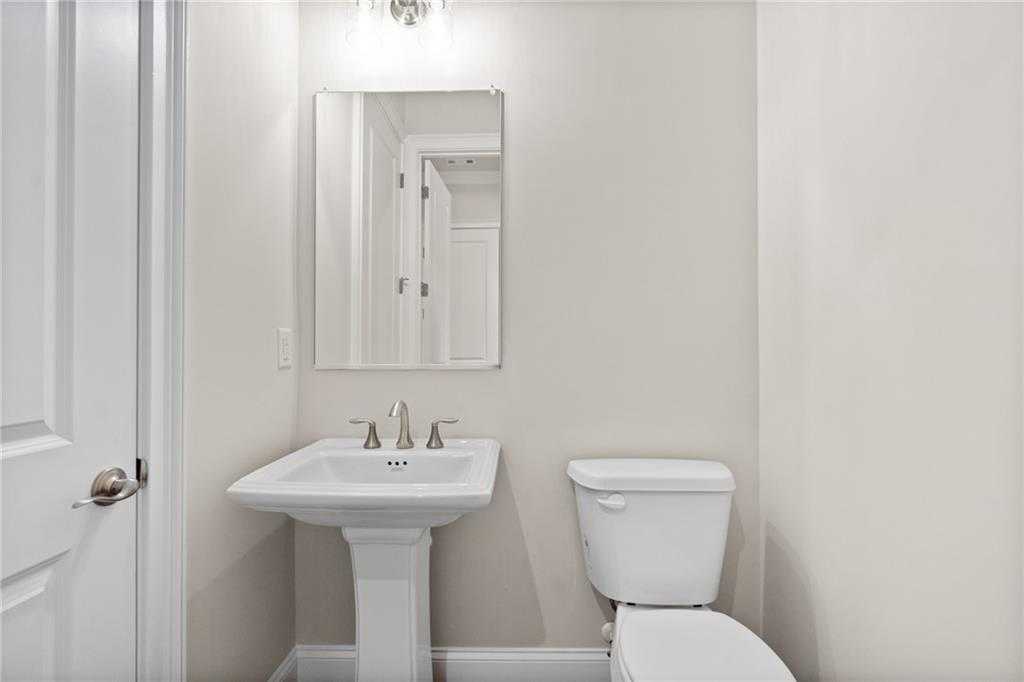 Elegant powder room with white pedestal sink, wall mirror, and toilet in Davidson Homes The Arlington A, East Cobb, Georgia