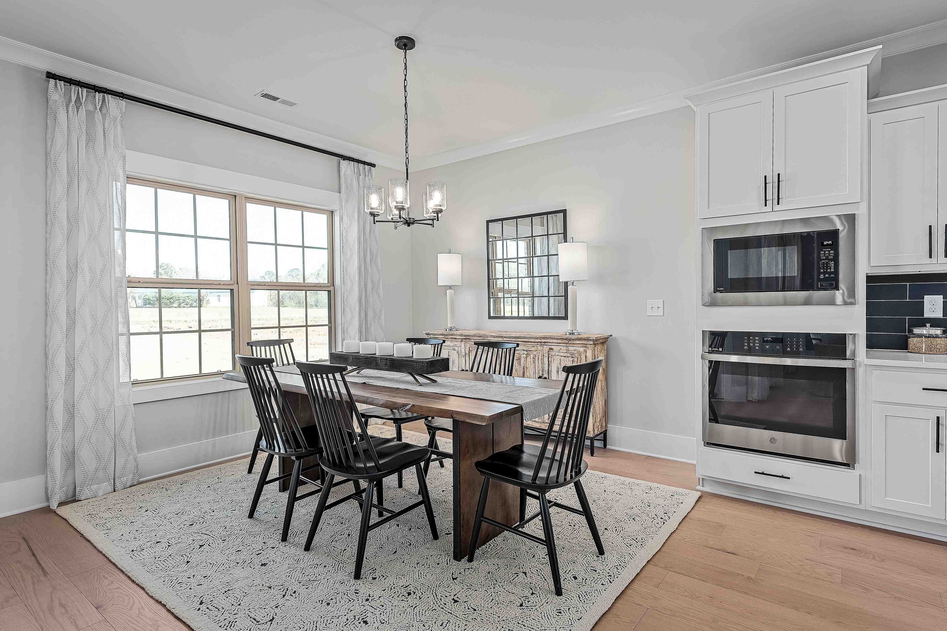 Elegant dining room in Cain Park Hartselle Alabama with wooden farmhouse table, black chairs, chandelier, buffet mirror, and white kitchen cabinets