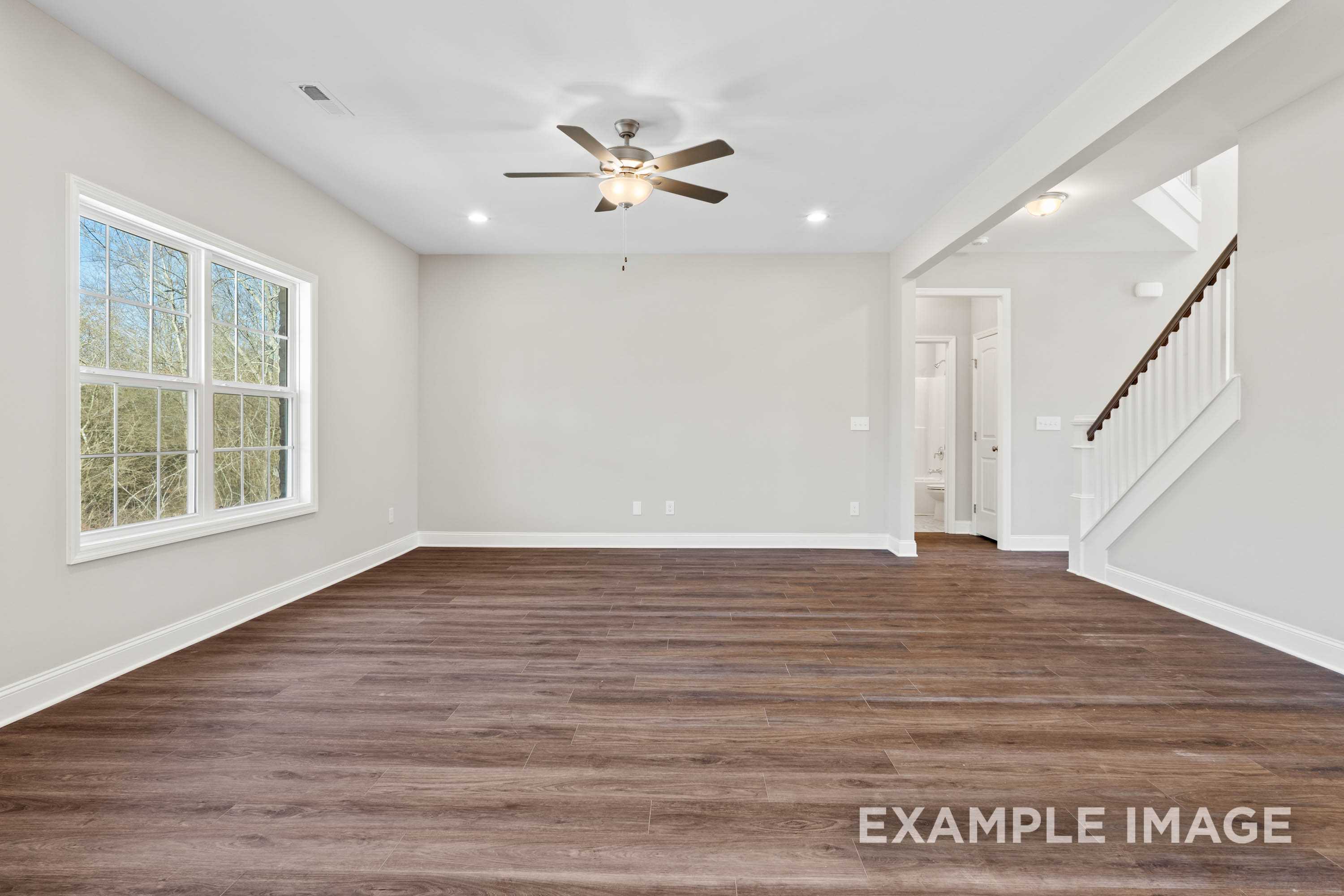 Spacious open living area in The Madison A Davidson Homes design with hardwood floors, large windows, ceiling fan, and staircase