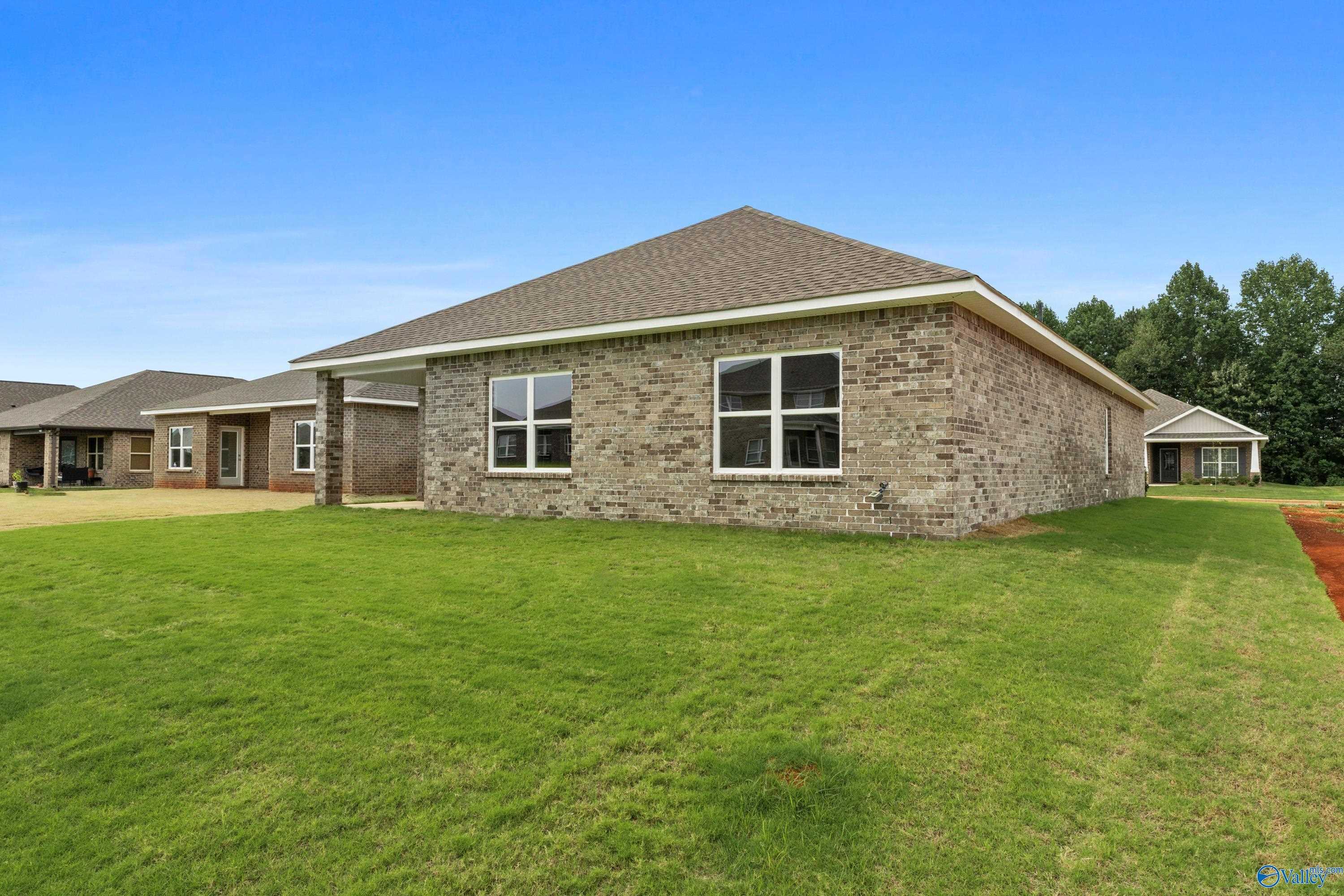 Single-story brick home with 2-car garage, large windows, shingled roof, and lush green lawn in Ricketts Farm, Athens, Alabama