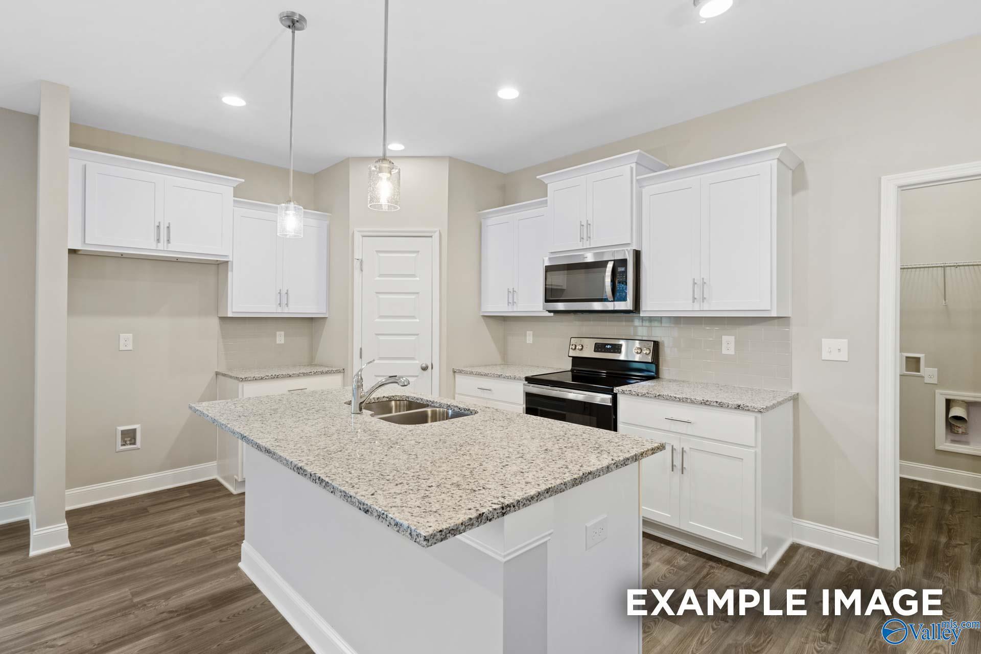 Modern kitchen with white cabinets, granite island, and stainless appliances in The Camilla D plan at The Retreat, Hartselle.