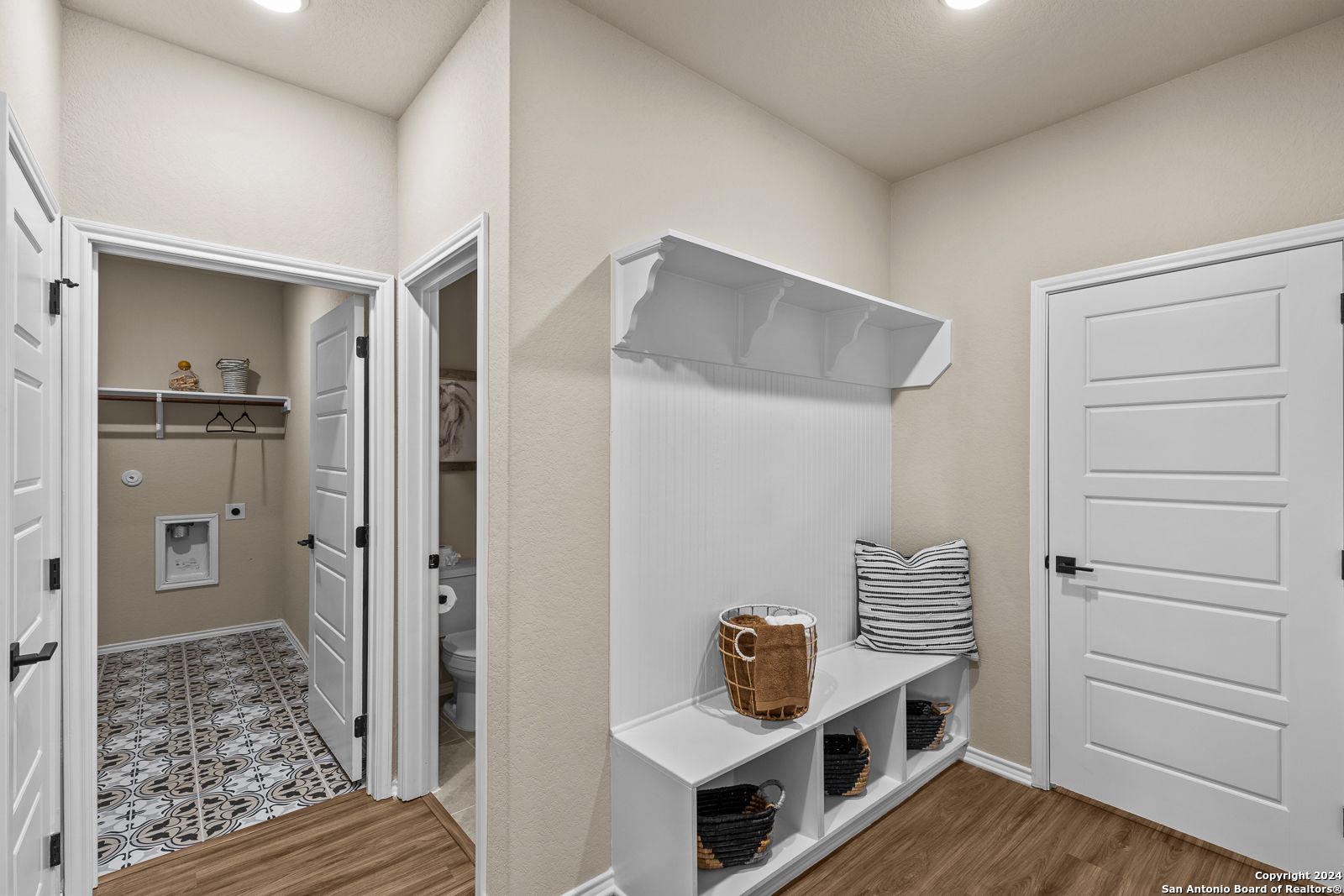 Functional mudroom with white built-in bench, coat hooks, cubbies, adjacent laundry and half bath in Davidson Homes The Douglas F, Bricewood San Antonio