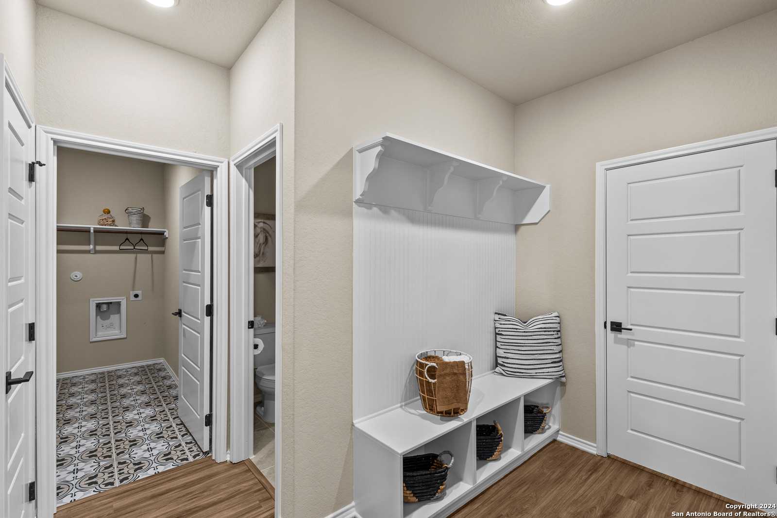 Functional mudroom with white built-in bench, coat hooks, cubbies, adjacent laundry and half bath in Davidson Homes The Douglas F, Bricewood San Antonio