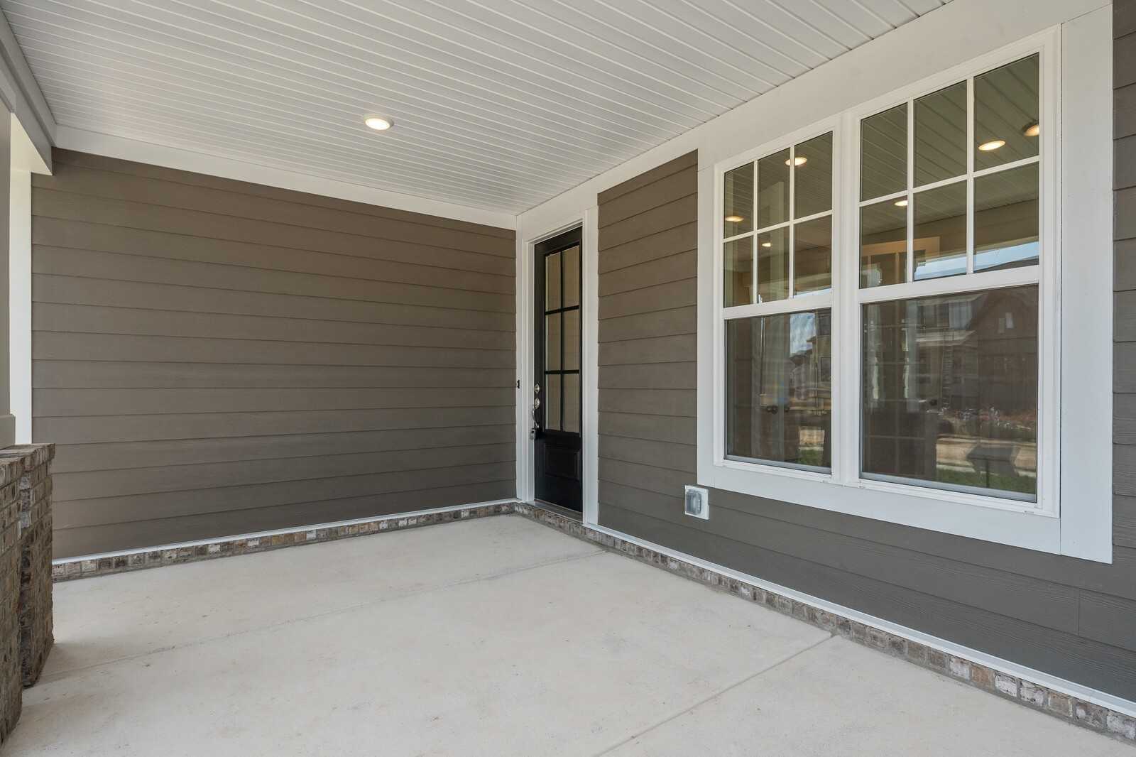 Inviting covered front porch with black glass door, sidelight windows, and gray siding in Davidson Homes The Hathaway, Murfreesboro