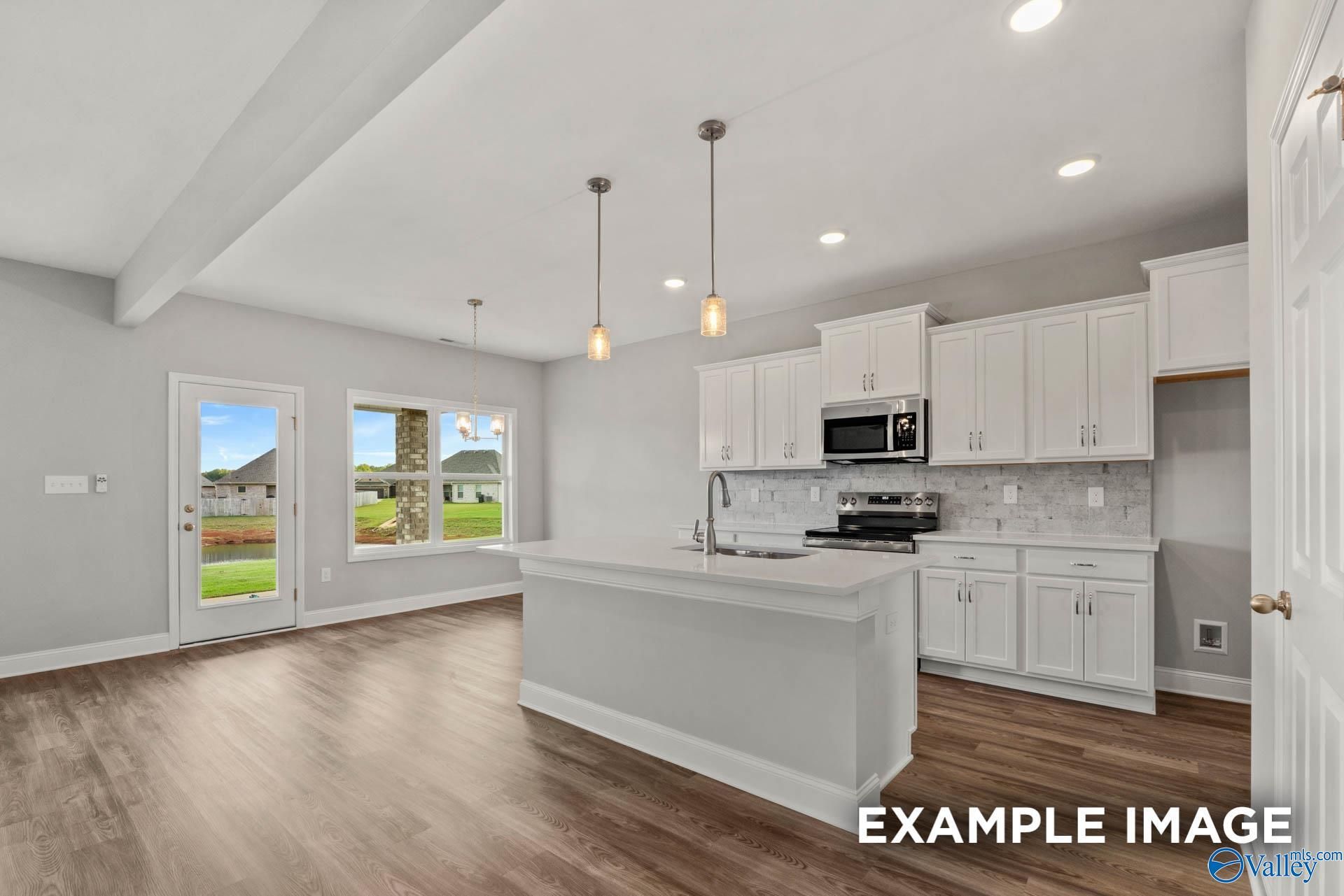 Modern white kitchen island with stainless microwave, pendant lights, and backyard views in The Shelby B home, Athens AL