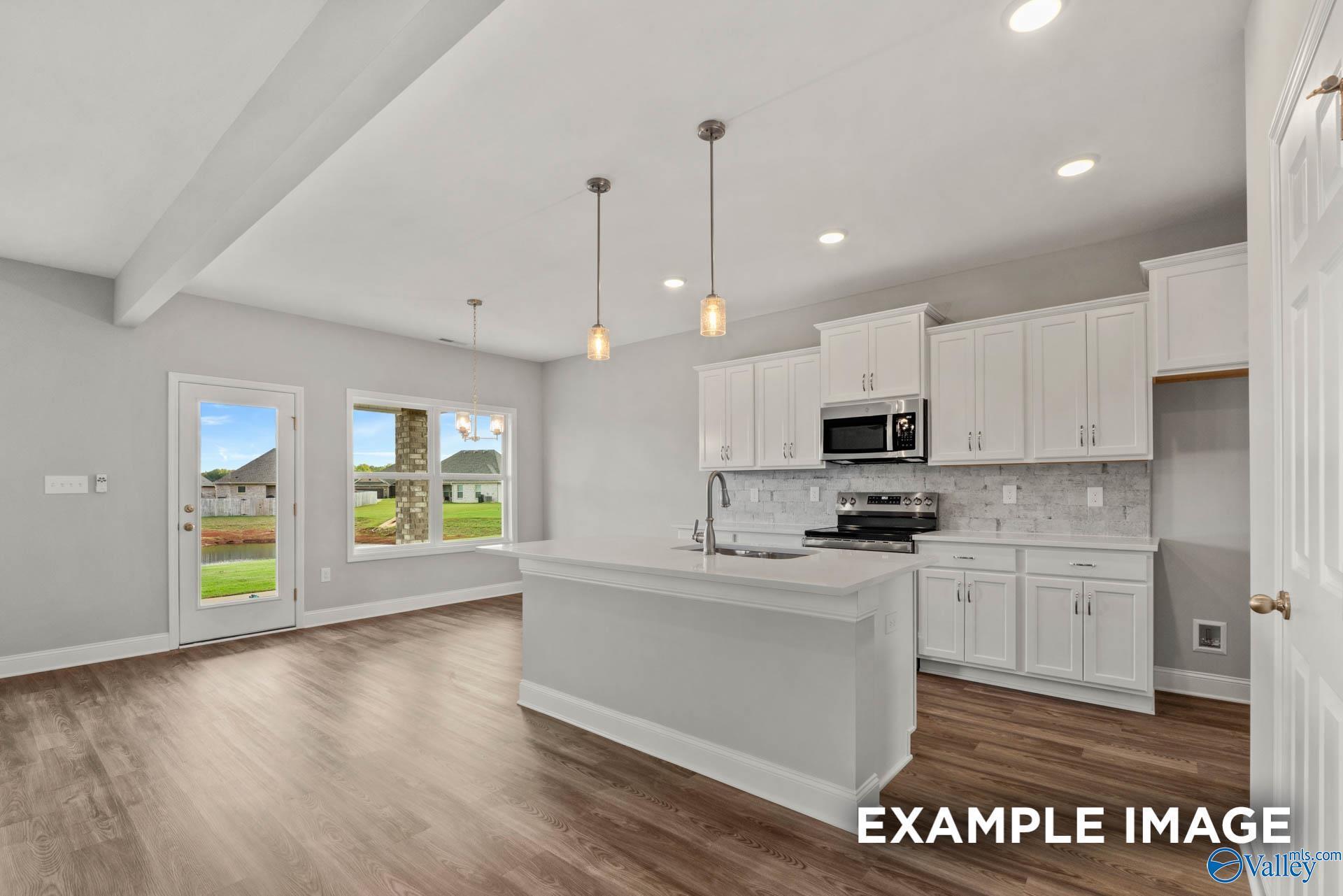 Modern white kitchen with island sink, stainless microwave, pendant lights, and backyard view in Davidson Homes Shelby B, New Market, AL